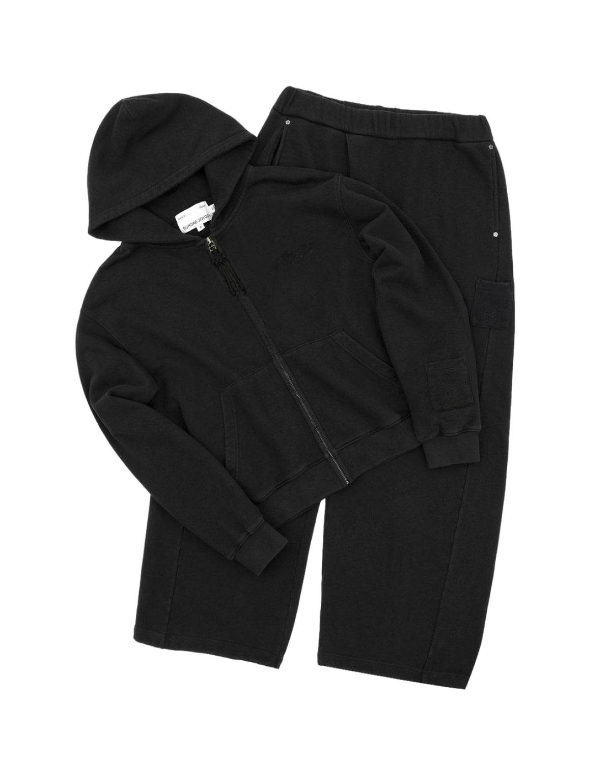 The BLACK WASH FLOWER KNOT ZIP UP by Sundae School is a black cotton zip-up hoodie featuring a hood, front pockets, and a signature Maehwa knot zipper pull, paired with matching black sweatpants with an elastic waistband. Both pieces are laid flat against a white background.