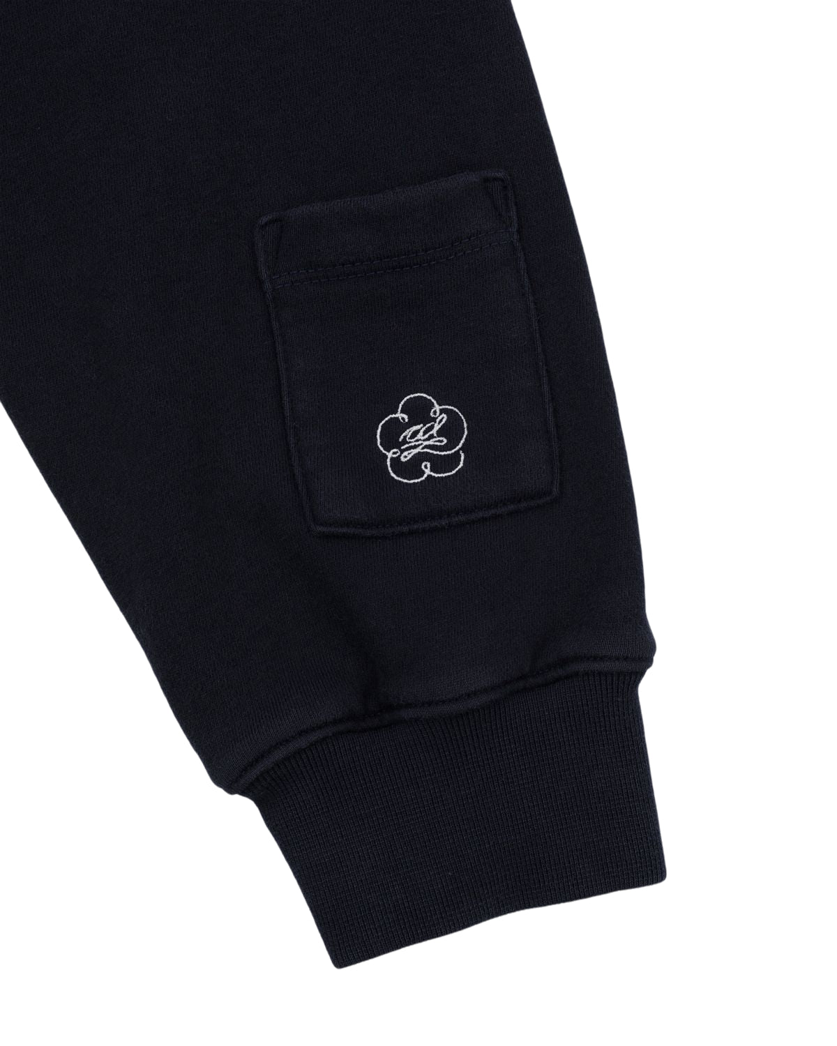 Close-up of a black sweatpant leg from Sundae School, featuring a small pocket adorned with a white embroidered flower motif inspired by the delicate Maehwa knot—a signature design element found in the NAVY WASH FLOWER KNOT ZIP UP. The ankle cuff is ribbed for added comfort.