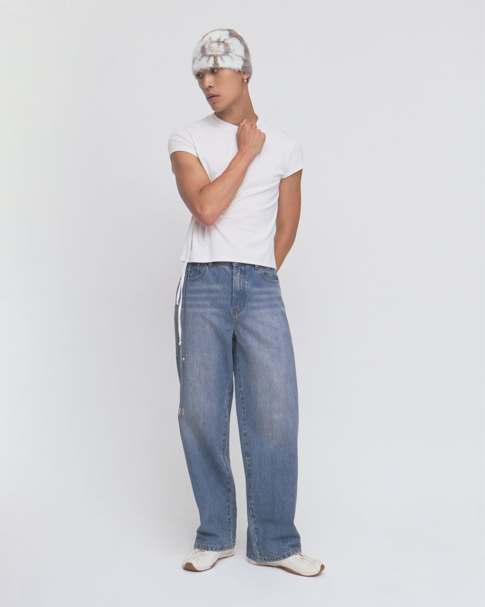 A person wearing a fitted white t-shirt, Sundae School MEDIUM BLUE FRESHMAN FIT DENIM jeans, white shoes, and a gray and white knit hat stands against a plain white background.