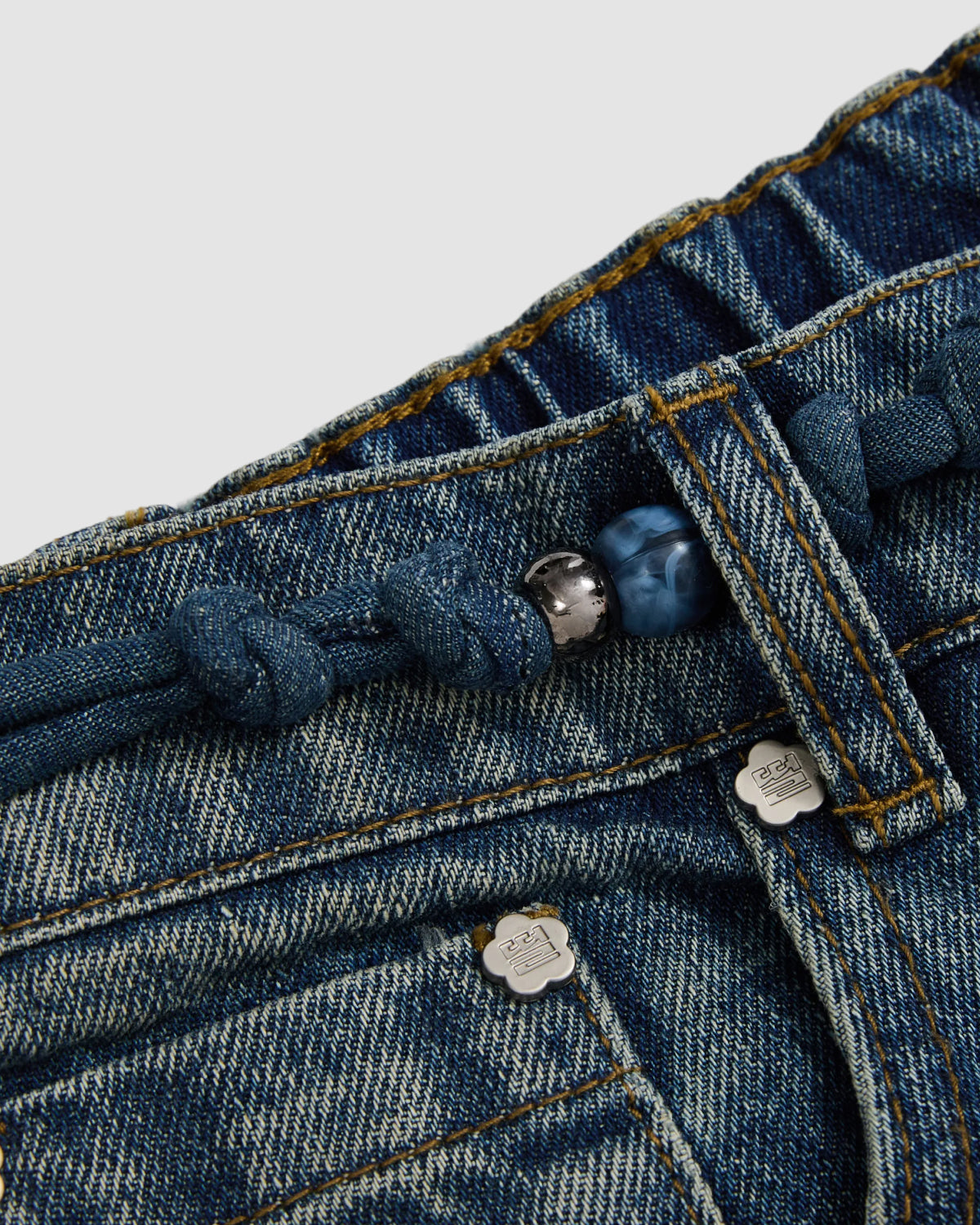 Close-up of Sundae School’s MEDIUM BLUE FRESHMAN FIT DENIM: relaxed straight-leg Korean jeans with a braided denim drawstring, Norigae-inspired bead detail, metal rivets, and textured stitching.