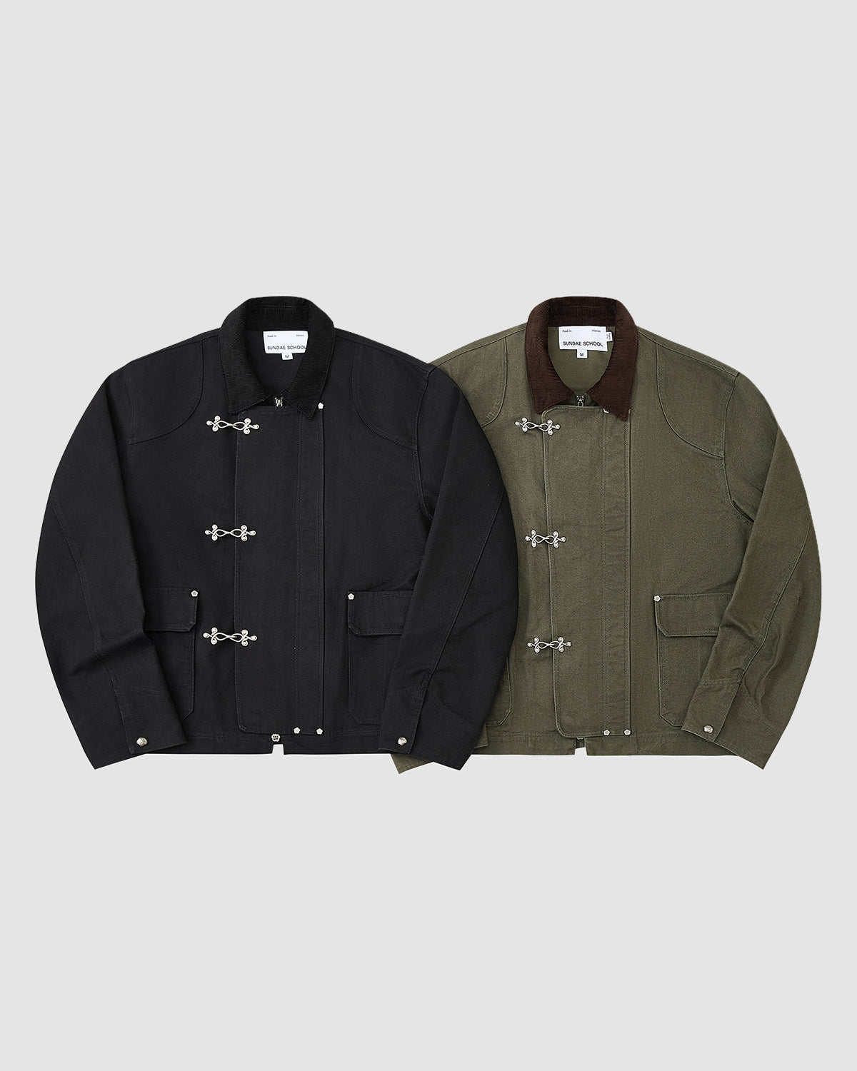 Two Sundae School workwear jackets are shown on a light grey background: left, a black vintage cotton jacket with silver clasps; right, the [PRE-ORDER] OLIVE FIREMAN CLASP JACKET in olive green with a brown collar and flap pockets.