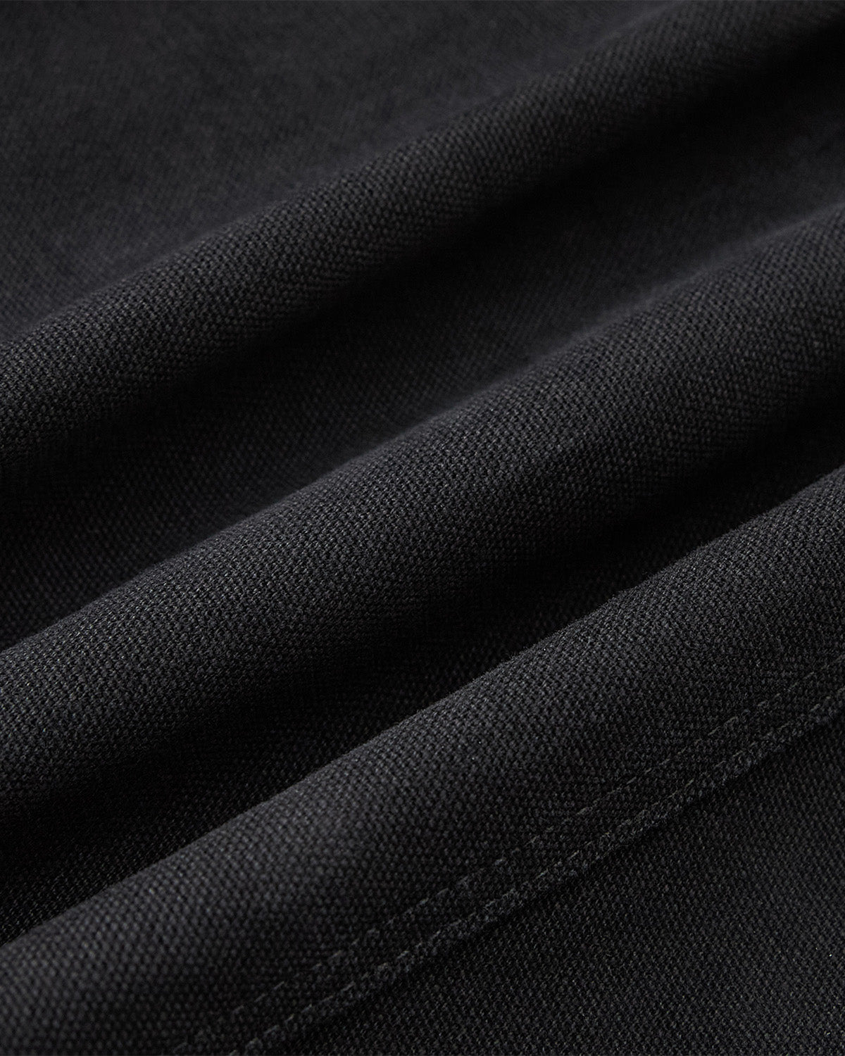 Close-up of folded black fabric from the Sundae School [PRE-ORDER] BLACK FIREMAN CLASP JACKET, showcasing its textured woven surface, soft cotton material, and fine seam stitching.