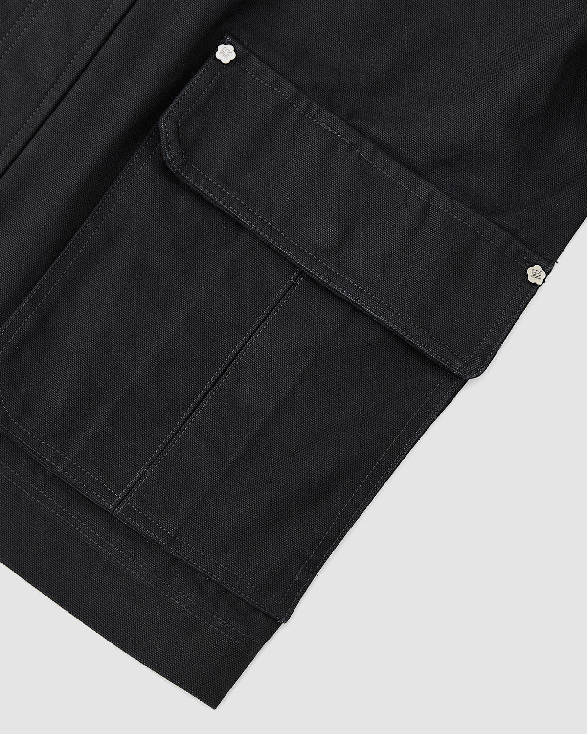 Close-up of the Sundae School [PRE-ORDER] BLACK FIREMAN CLASP JACKET pocket, featuring a flap with two silver snaps, detailed stitching, and a clean, structured design against a light background.