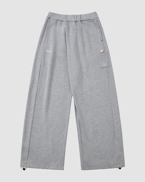 The HEATHER GREY WRAP SWEATBAJI by Sundae School are wide-leg, light gray unisex cotton pants with an elastic waistband, zipper fly, two side pockets, a thigh patch pocket, and small embroidered details at the pockets and hems.