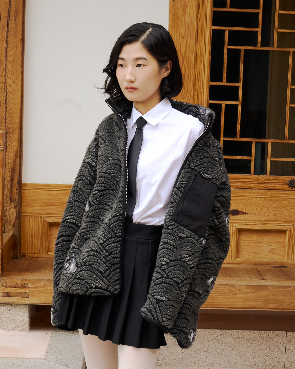 Person wearing a Sundae School Black Wave fleece over a school uniform in front of a traditional Korean hanok.