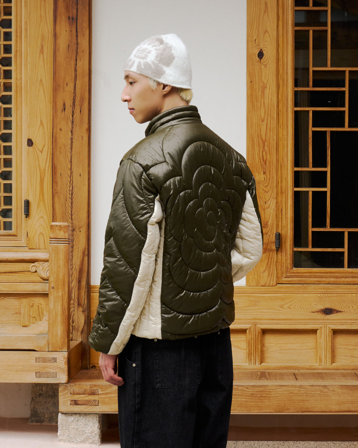 A person wearing Sundae School’s OLIVE OATMEAL MOCHI SPIRAL PUFFER stands with their back to a decorative wooden door.