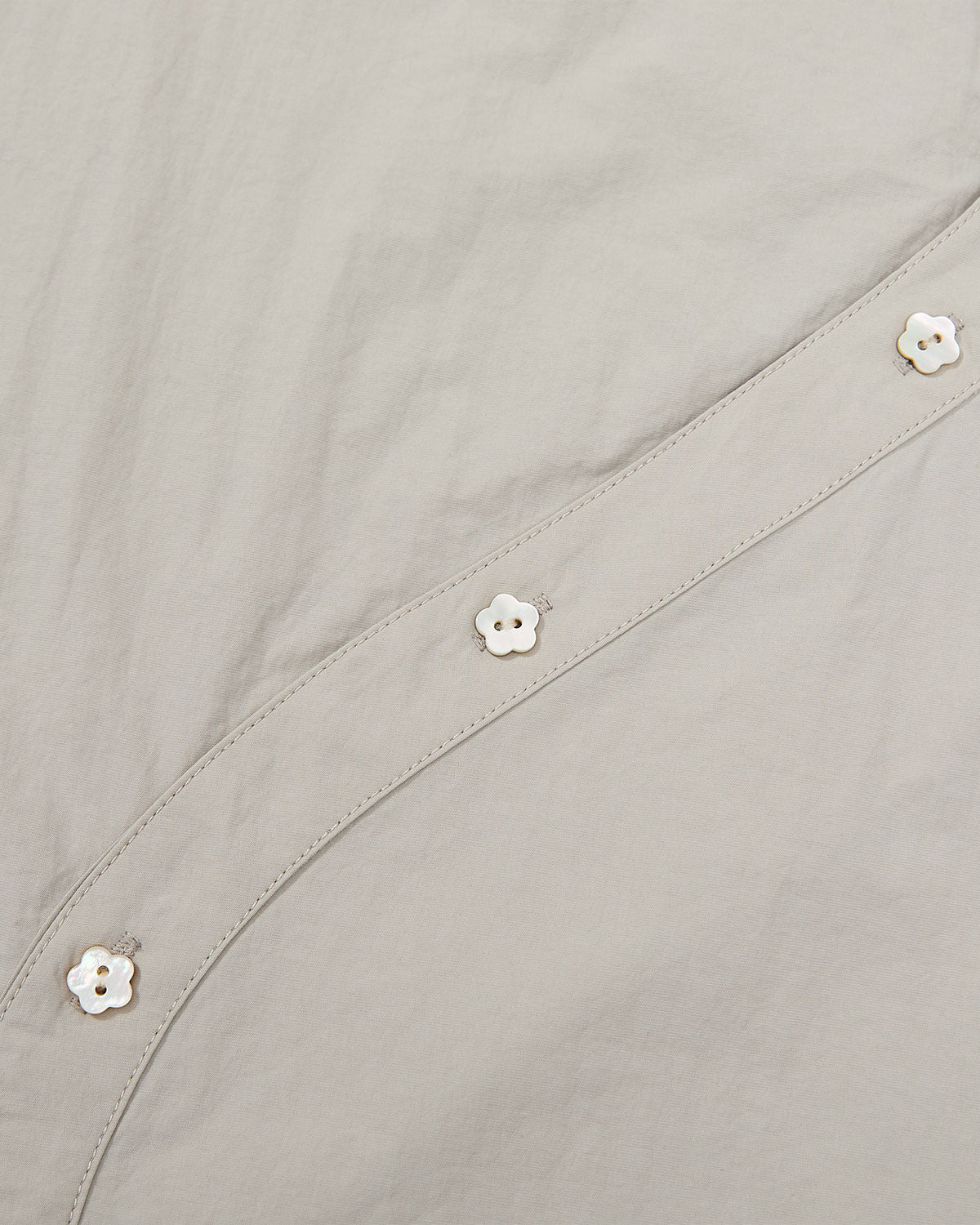 Close-up of three white flower-shaped mother-of-pearl buttons along the curved asymmetrical placket of the Gray Yin Yang Short Sleeve Shirt.