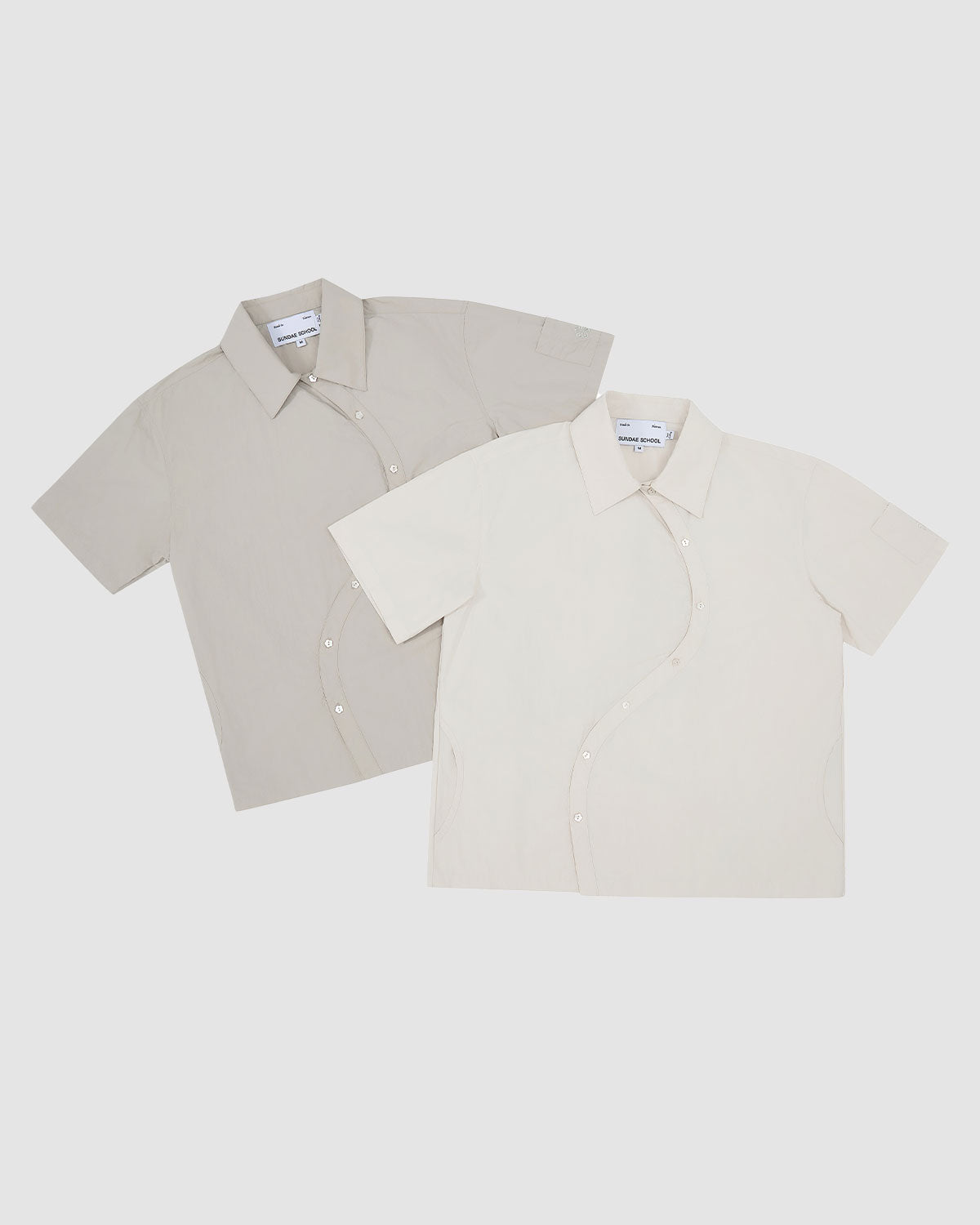 Flat lay of two Gray Yin Yang Short Sleeve Shirts - one in light gray and one in off-white - showing the asymmetrical curved button placket design on both colorways.
