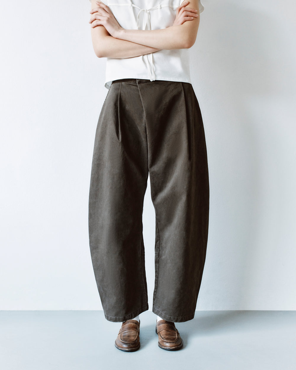 A person wearing dark olive SOIL HANBOK CHINO PANTS in a barrel-fit style with pleats and brown leather loafers.