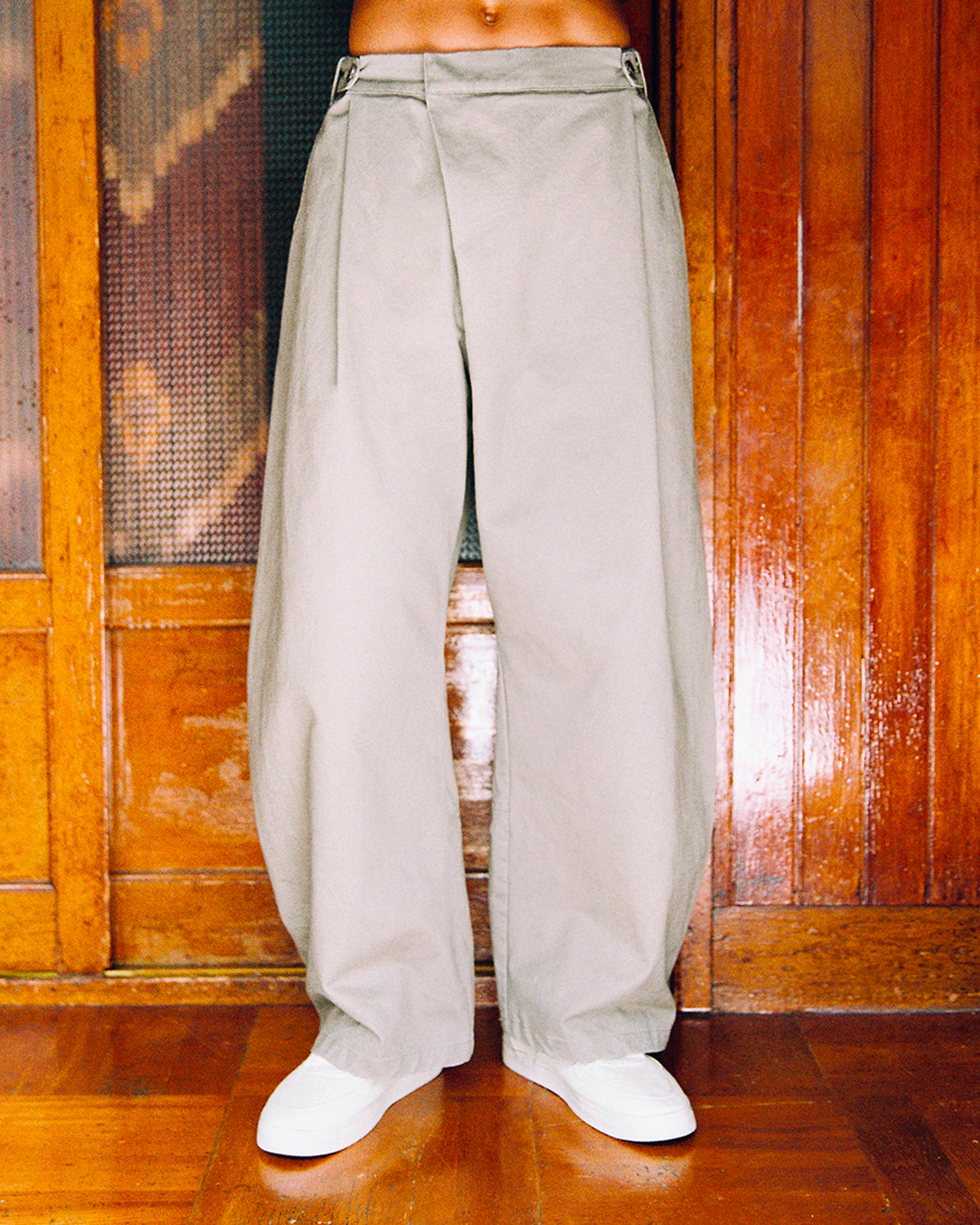 Light gray, wide-leg, wrap-front STONE KIEF HANBOK CHINO PANTS worn with white sneakers.