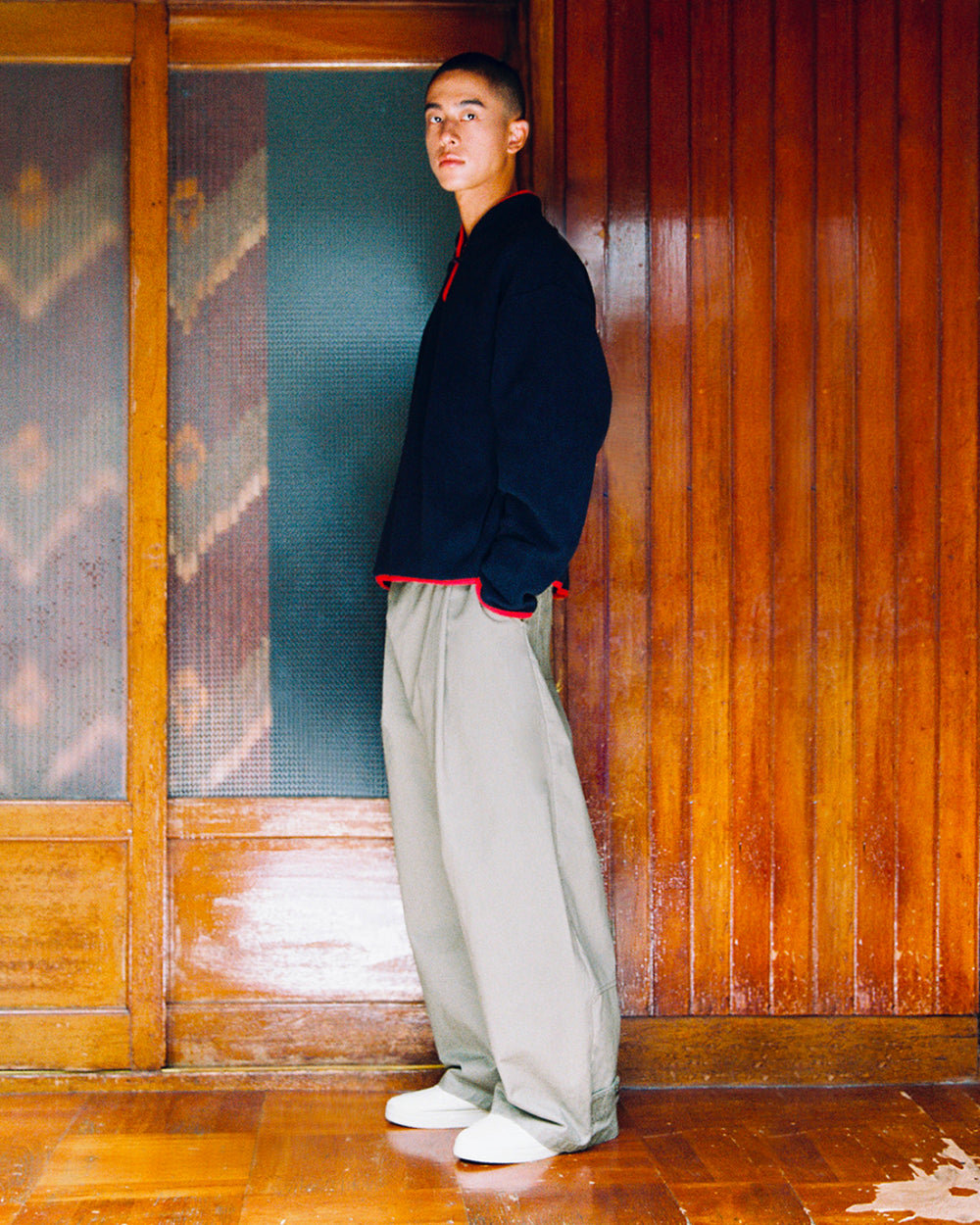 A person stands wearing a dark pullover with red trim and light gray STONE KIEF HANBOK CHINO PANTS in a barrel-fit.