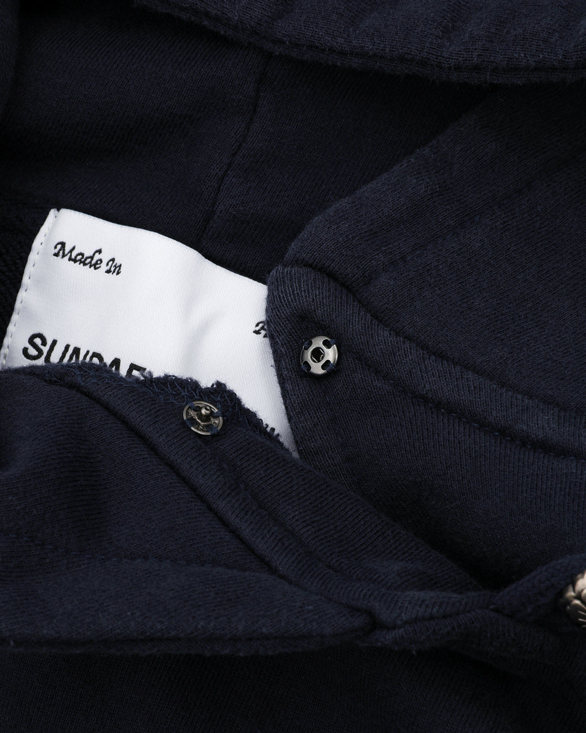 A close-up of the NAVY WASH HANBOK HOODIE by Sundae School shows its oversized hood, metal snap button, and a partially visible white label reading 