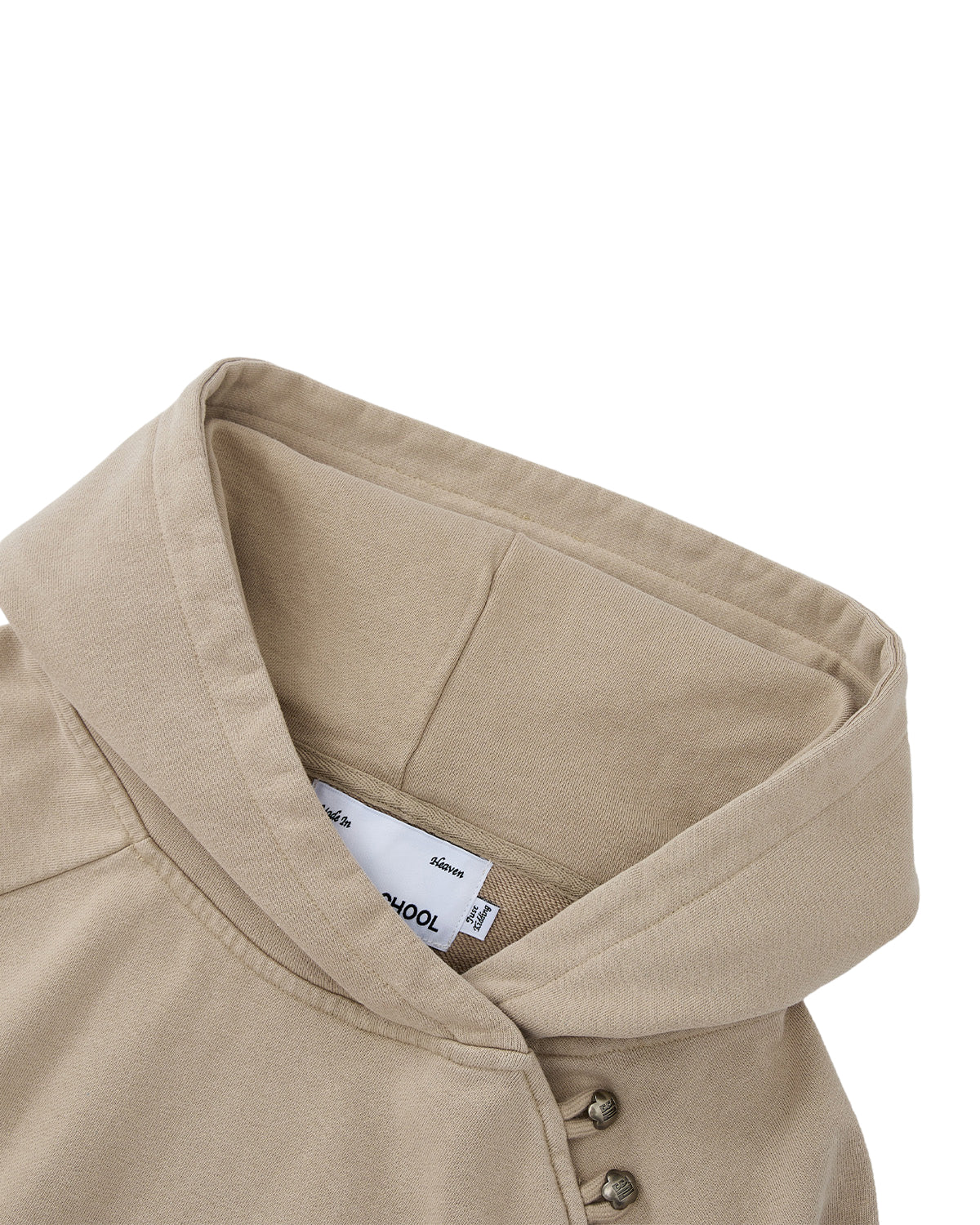 A close-up of Sundae School’s TAUPE HANBOK HOODIE showcases its beige color, distinctive wide collar, and asymmetric hood closure with metal snap buttons on one side, as well as a visible white tag inside the neckline. The signature stash pocket enhances both the style and functionality of this unique piece.