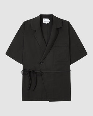 The BLACK HANBOK LINEN SHIRT by Sundae School is a black, short-sleeve cotton-linen blend with a notched collar, chest pocket, single button closure, and side tie—styled like a modern hanbok shirt on a light grey background.