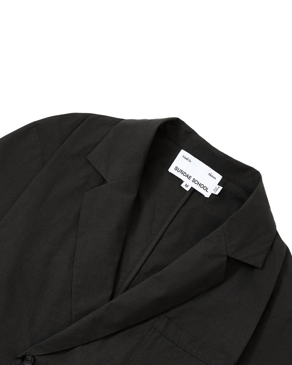 Close-up of the BLACK HANBOK LINEN SHIRT by Sundae School. Drawing inspiration from the refined minimalism of a summer hanbok, it features smooth, slightly matte fabric reminiscent of modern cotton linen hanbok materials. The inner label displays “Sundae School” with size L printed below.