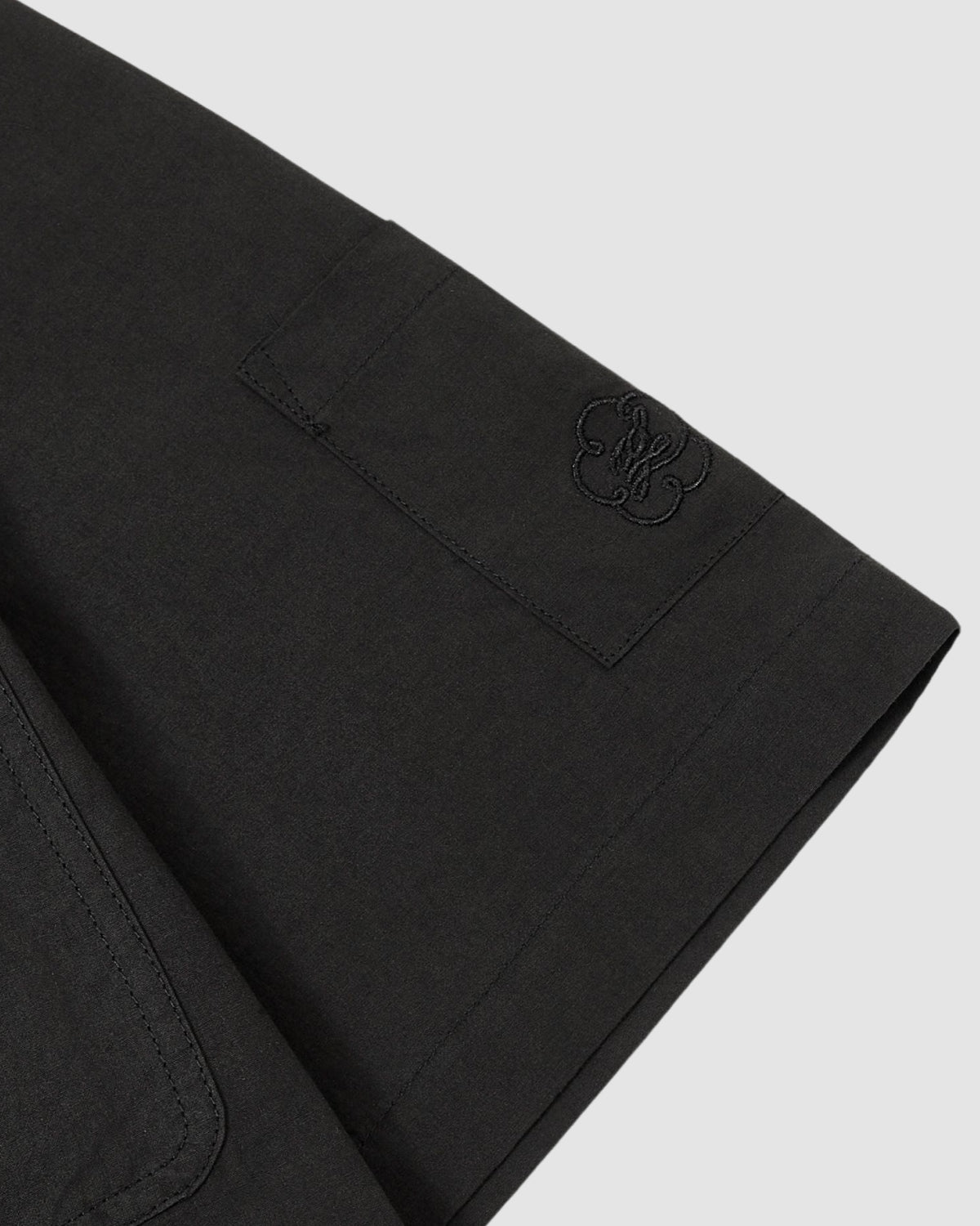 Close-up of the Sundae School BLACK HANBOK LINEN SHIRT sleeve, showing a neatly stitched pocket and subtle black embroidered logo, crafted from a comfortable cotton linen blend, set against a plain light grey background.