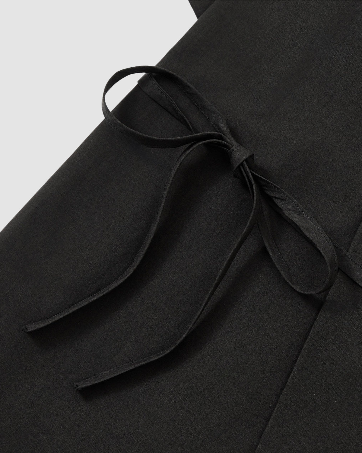 Close-up of the BLACK HANBOK LINEN SHIRT by Sundae School, featuring a thin matching waist tie knotted into a neat bow, shown against a light grey background.