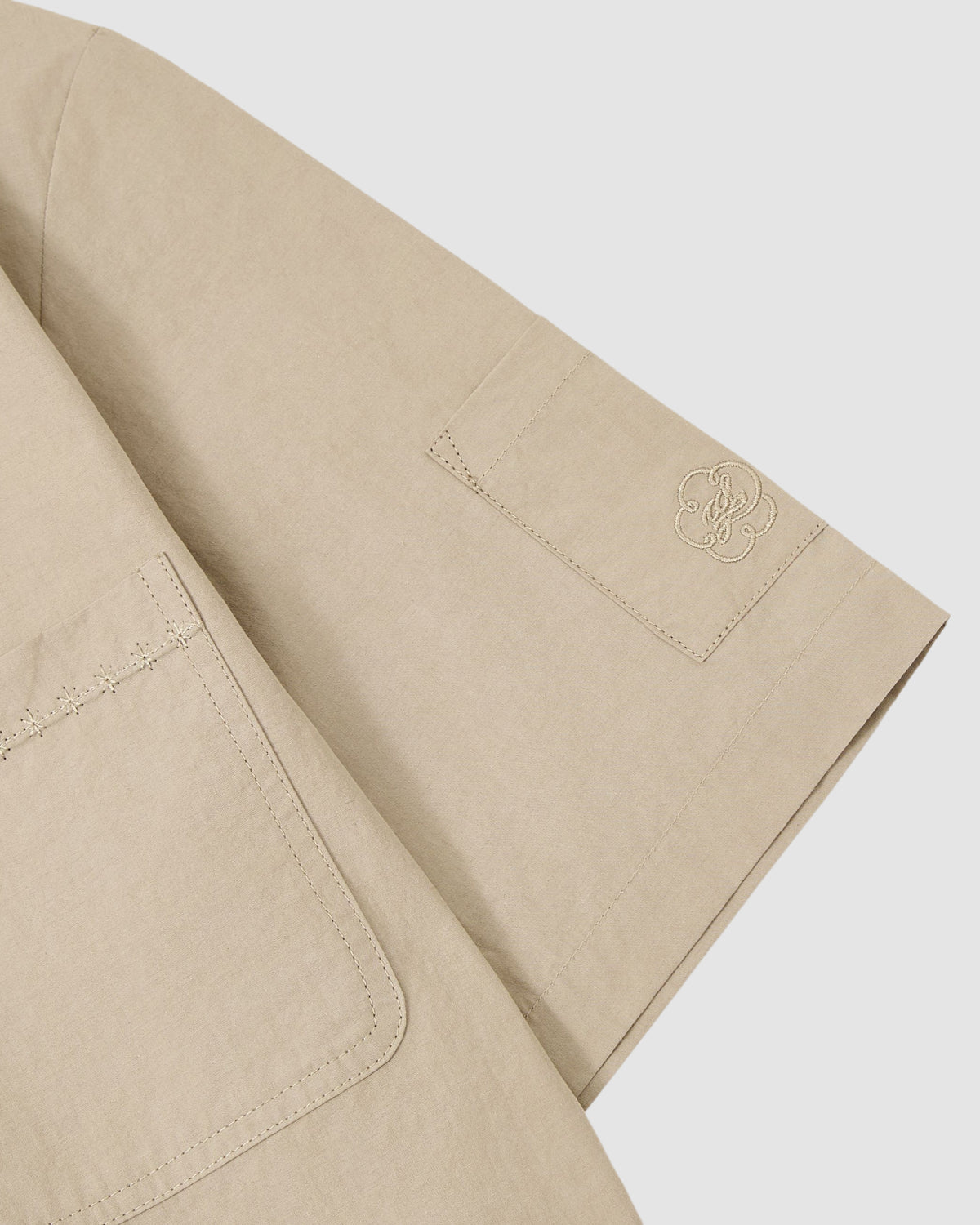 Close-up of the Sundae School WHEAT HANBOK LINEN SHIRT, featuring a beige cotton-linen blend, large pocket, subtle sleeve logo embroidery, and smooth matte texture.