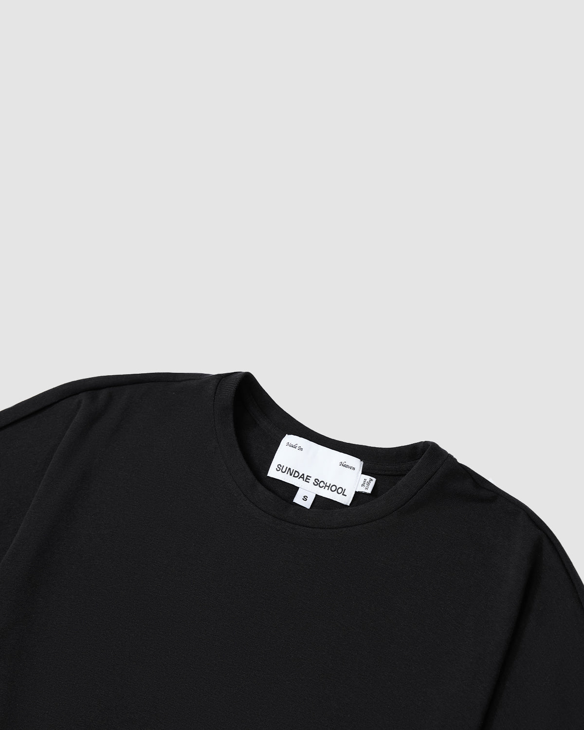 A close-up of the BLACK BAERAE T-SHIRT by Sundae School, laid flat on a light gray background, highlights the neckline and collar tags—drawing inspiration from the traditional Korean overcoat, durumagi.