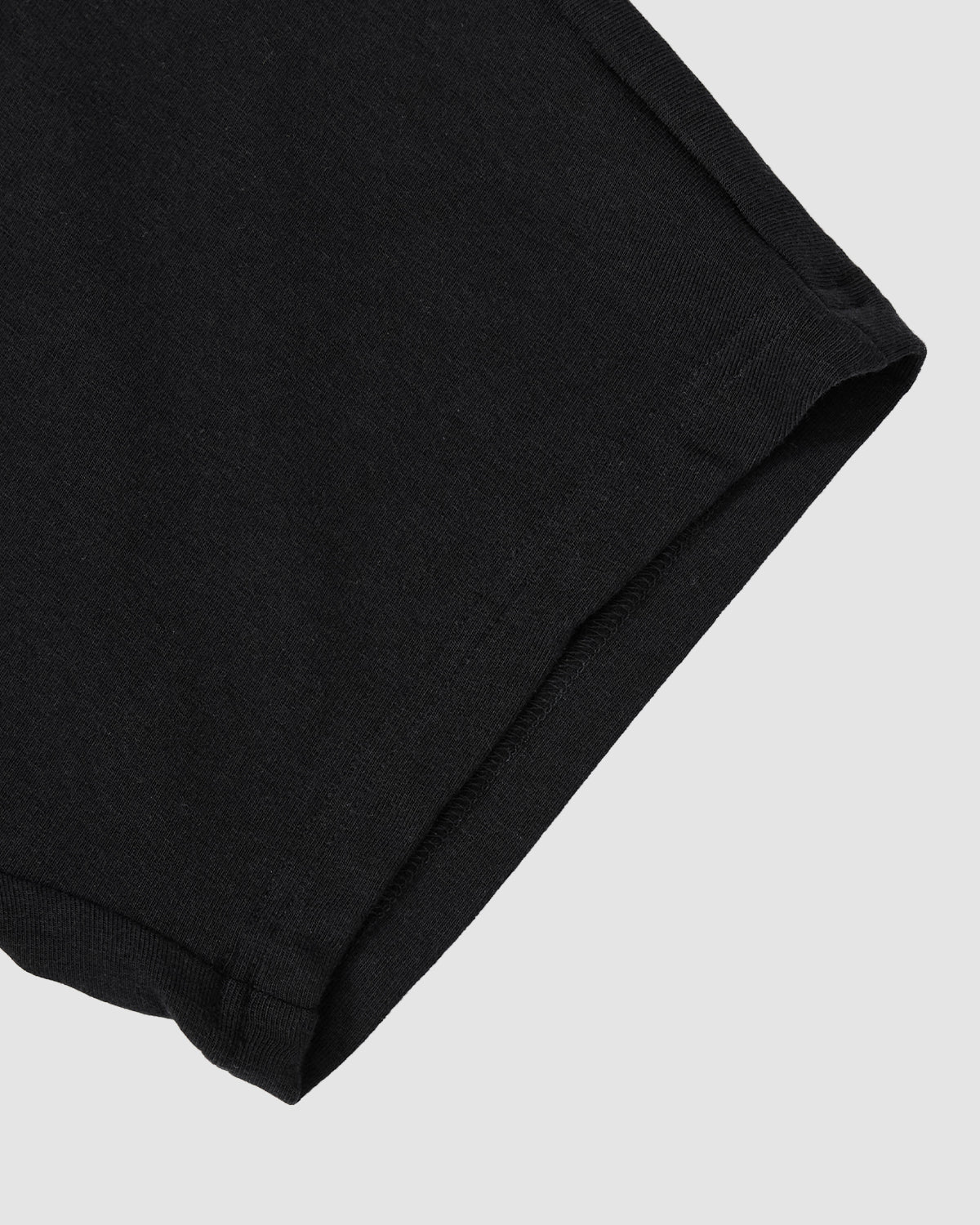 Close-up of the hem of the BLACK BAERAE T-SHIRT by Sundae School, inspired by traditional Korean overcoat designs. Set against a light gray background, the fabric looks soft and subtly textured.