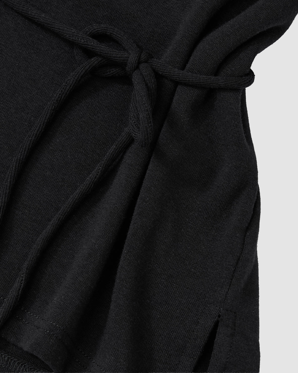 Close-up of the BLACK BAERAE T-SHIRT by Sundae School, a black fabric piece with a tied waist belt and visible hem stitching, inspired by the traditional Korean durumagi, shown against a light gray background.