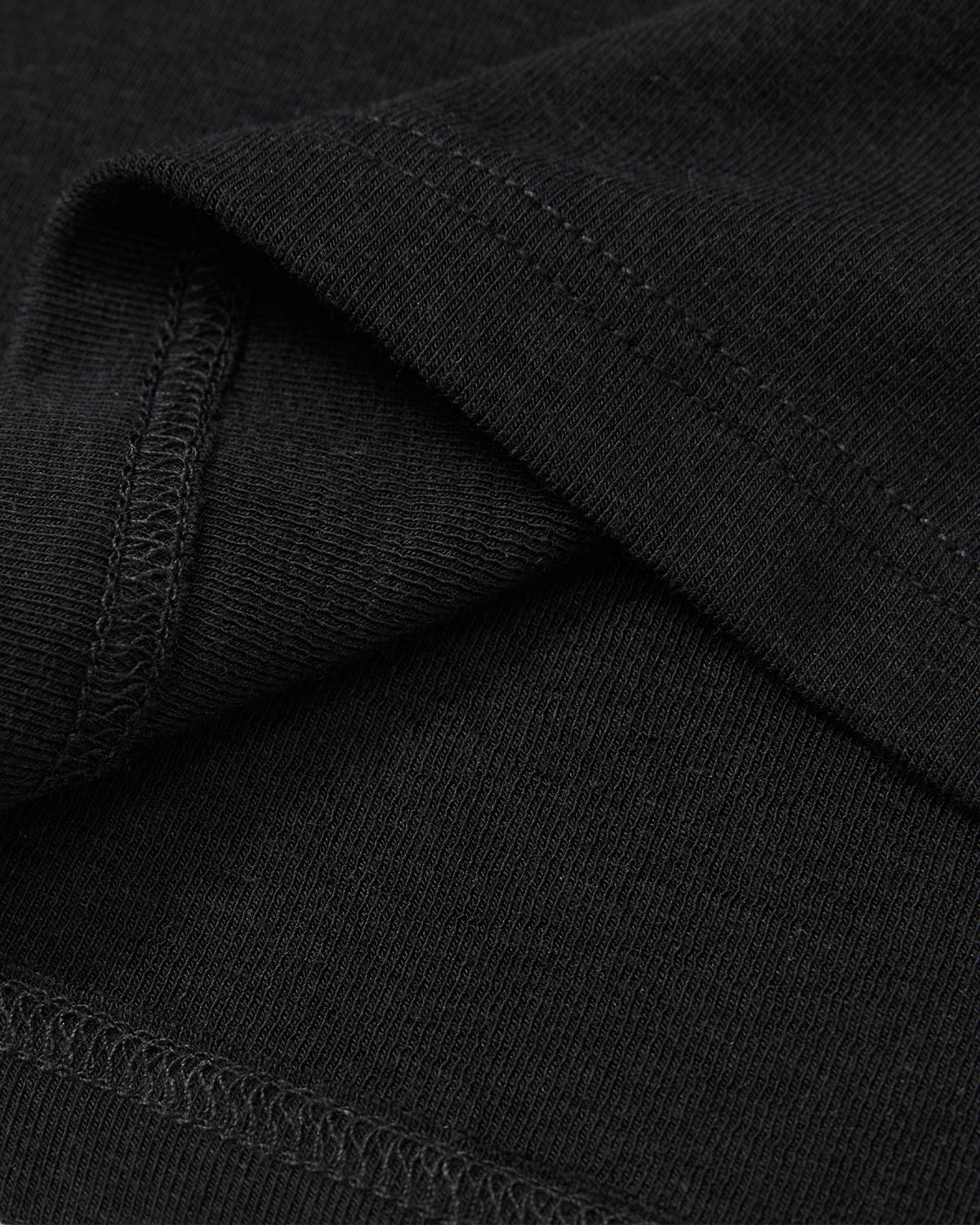 Close-up of the BLACK BAERAE T-SHIRT by Sundae School, featuring black fabric with visible stitching and a folded hem, echoing the texture and detailing of a traditional Korean overcoat like the durumagi.