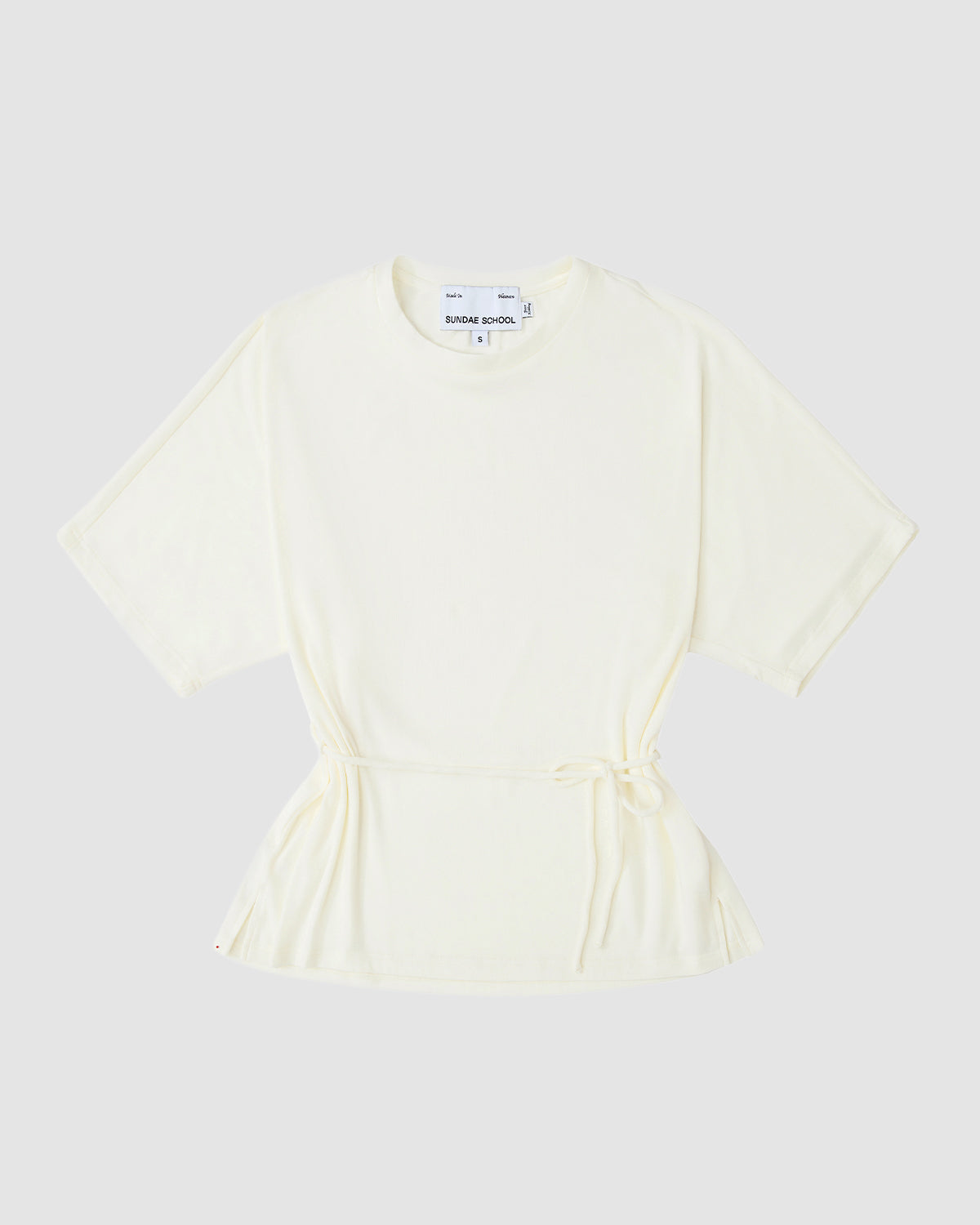 The IVORY BAERAE T-SHIRT by Sundae School, inspired by the traditional Korean durumagi, features short sleeves, a round neck, drawstring waist, and an off-white hue. It is laid flat on a light gray background with a white label at the neckline.