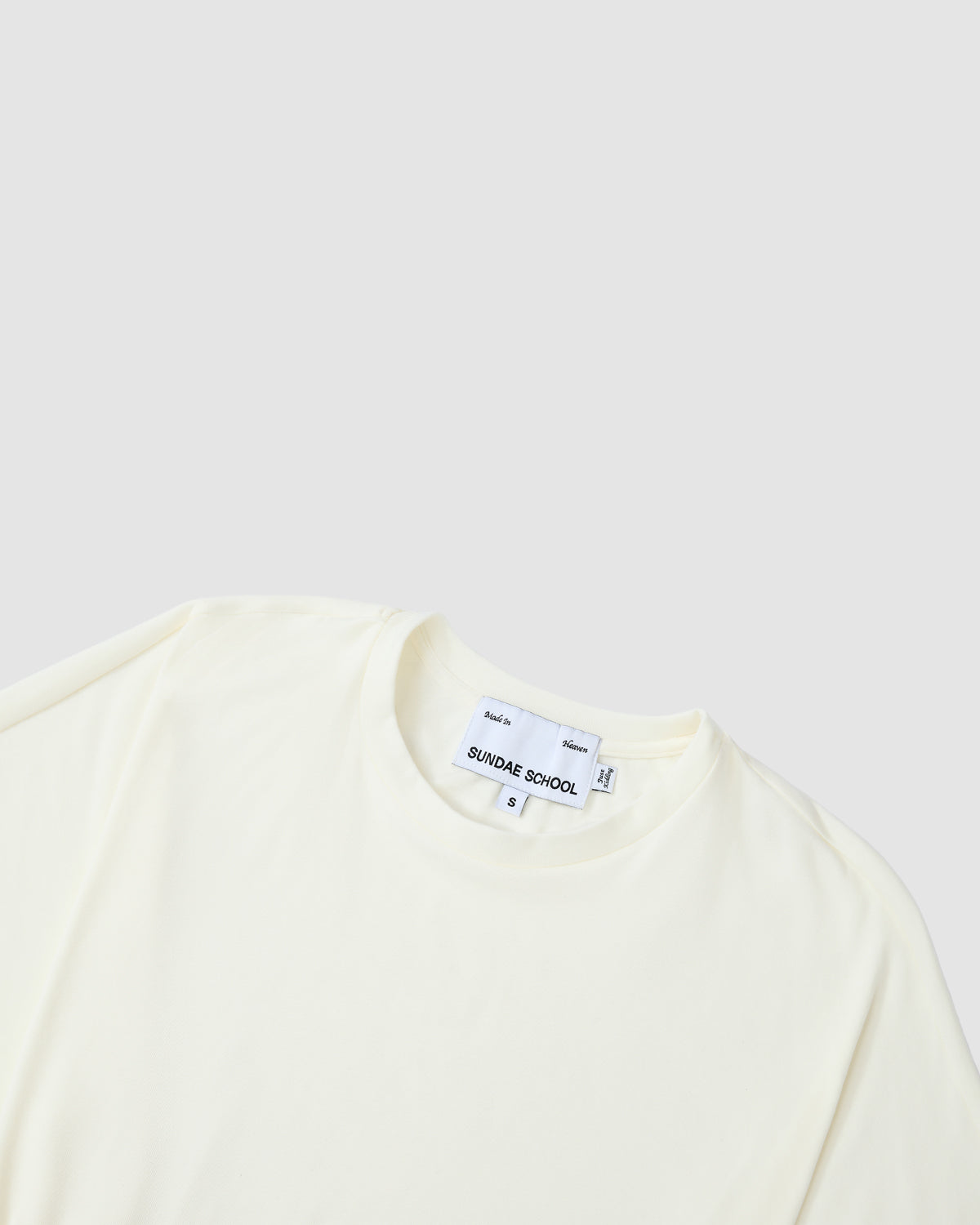 The IVORY BAERAE T-SHIRT by Sundae School lays flat on a light gray background, featuring a visible neck tag. This classic crewneck subtly nods to the traditional Korean durumagi overcoat.