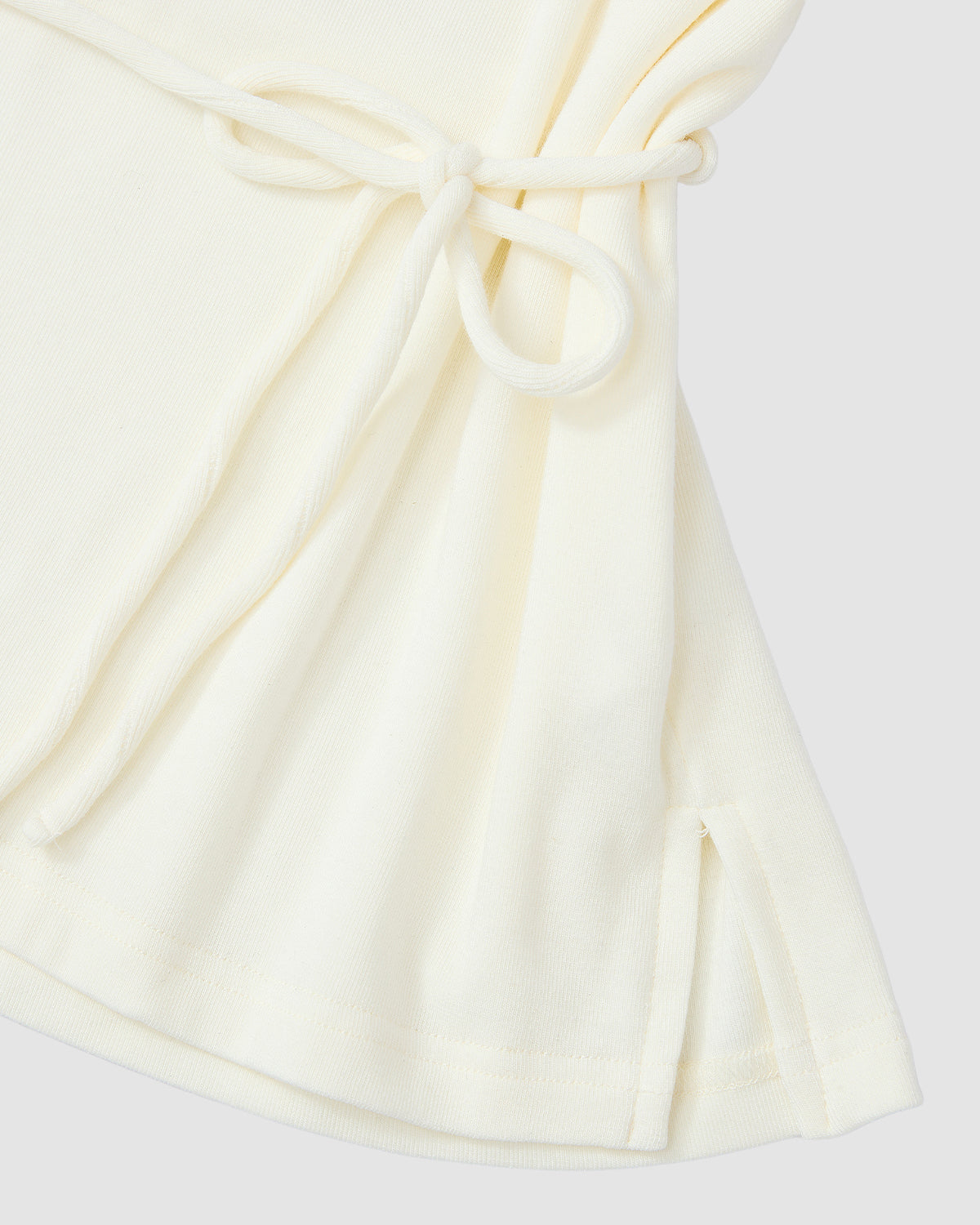 Close-up of the Sundae School IVORY BAERAE T-SHIRT, featuring soft, slightly textured cream fabric with a side tie detail and small slit at the hem, inspired by the traditional Korean overcoat durumagi.