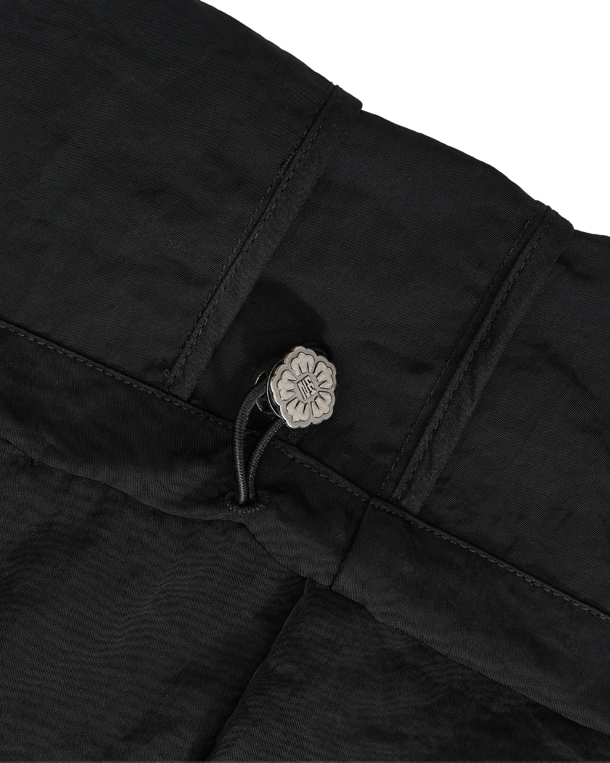 Close-up of black textured fabric with a small silver floral button and black cord detail on a white background.