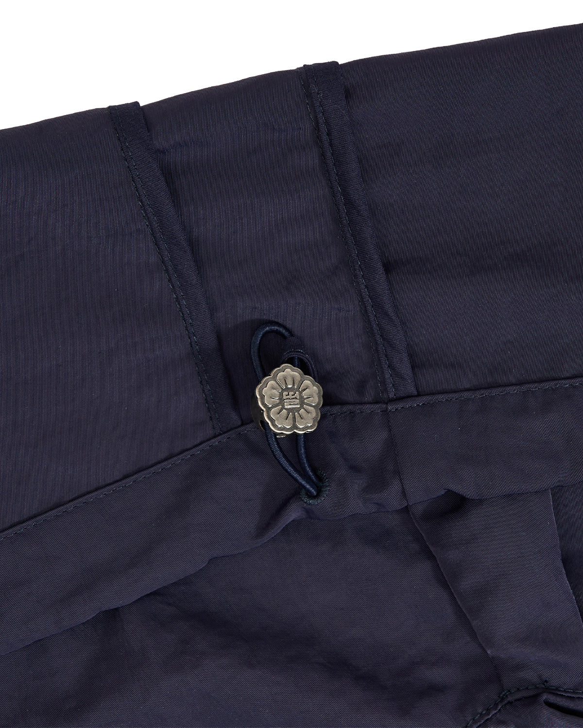 Close-up of dark navy fabric with a small metallic flower-shaped button and dark cord detail.