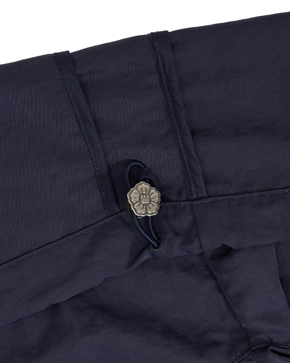 Close-up of dark navy fabric with a small metallic flower-shaped button and dark cord detail.