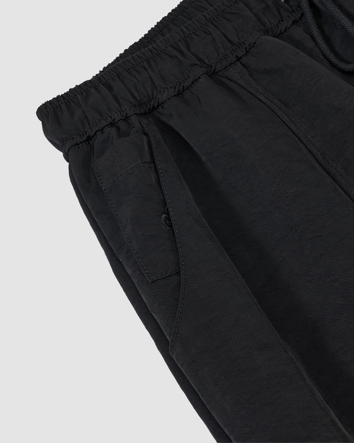 Close-up of Sundae School's BLACK HANBOK BALLOON TRACK PANTS, showcasing an elastic waistband, visible drawstring, and side pocket details with a curved barrel silhouette against a light gray background.