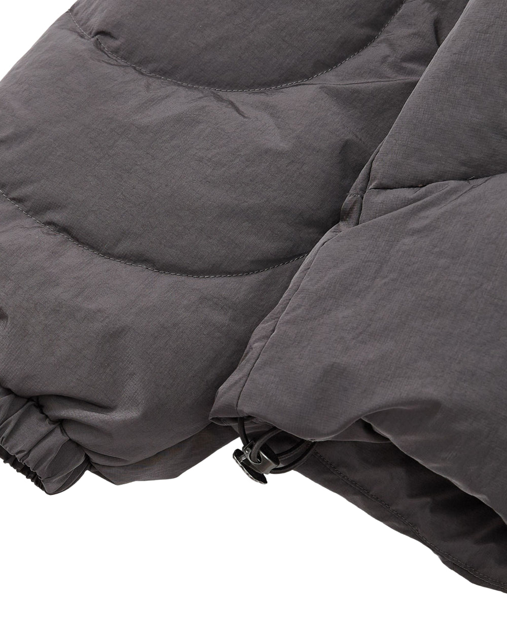 Close-up of the Sundae School CHARCOAL HEAVYWEIGHT MOCHI PUFFER, featuring a dark gray sleeve with an elasticated wrist and a drawstring cord at the hem for an adjustable fit.
