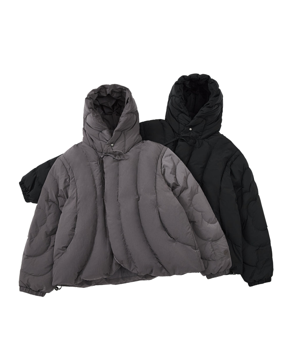 Two CHARCOAL HEAVYWEIGHT MOCHI PUFFER jackets from Sundae School, one in gray and one in black, are laid flat with their edges overlapping. Each jacket showcases a quilted design with curved stitching and hoods equipped with adjustable drawstrings. These heavyweight puffers are filled with cozy duck down for extra warmth.