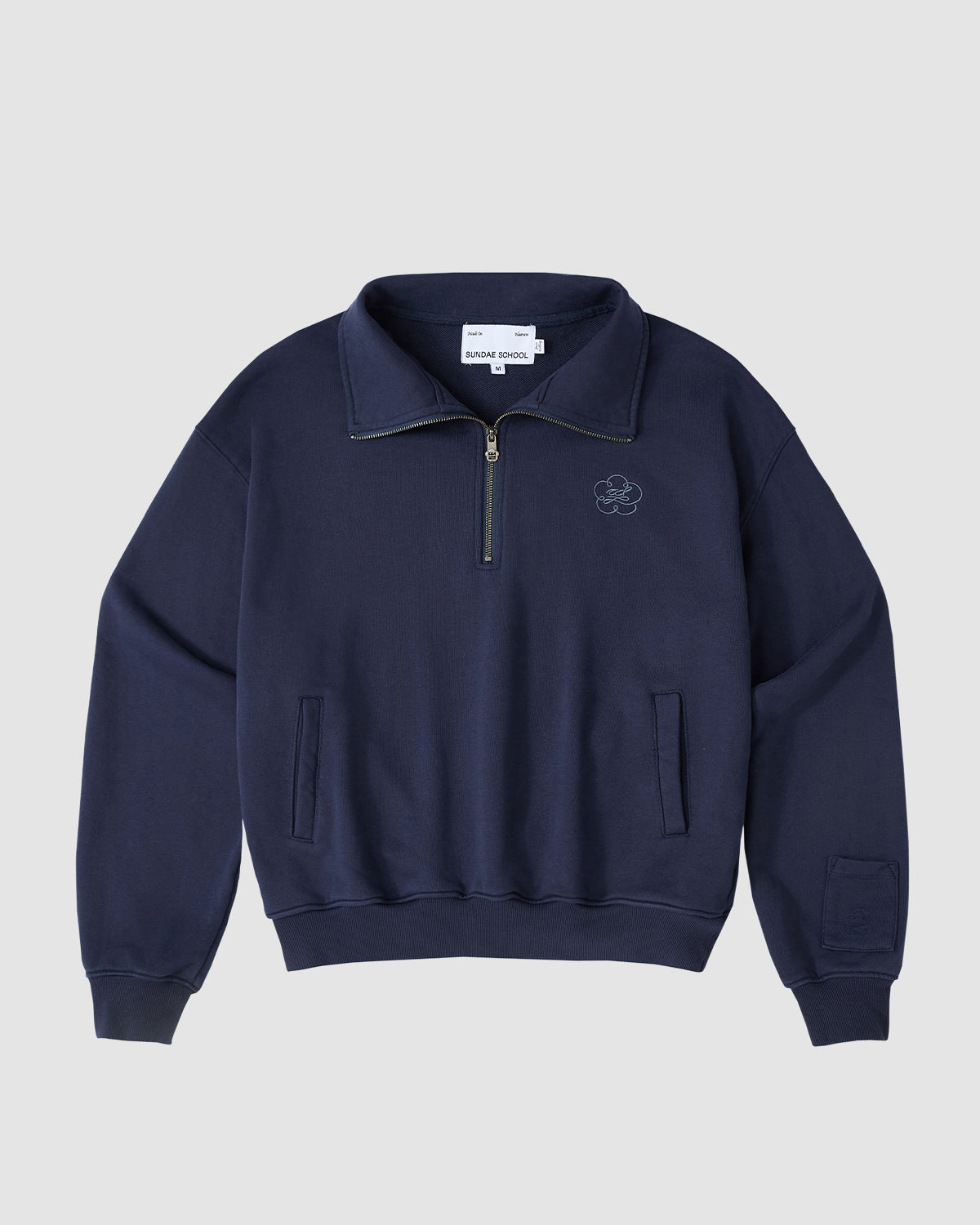 The Sundae School NAVY HESTER QUARTER ZIP is a vintage cotton pullover with a high collar, oversized quarter zip, two front pockets, ribbed cuffs and hem, and an embroidered logo on the left chest, shown on a light gray background.