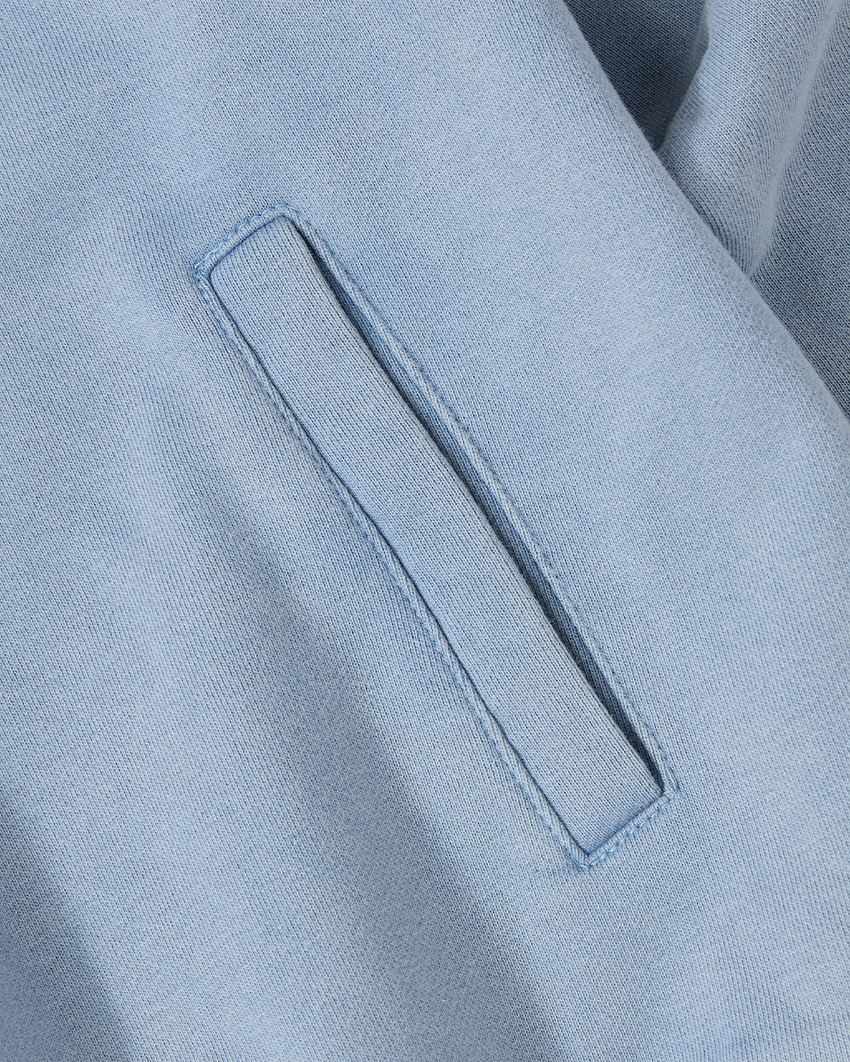 Close-up of the SKY BLUE HESTER QUARTER ZIP by Sundae School, showing soft, slightly textured cotton with a vintage light blue fade and a neatly sewn horizontal stash pocket.