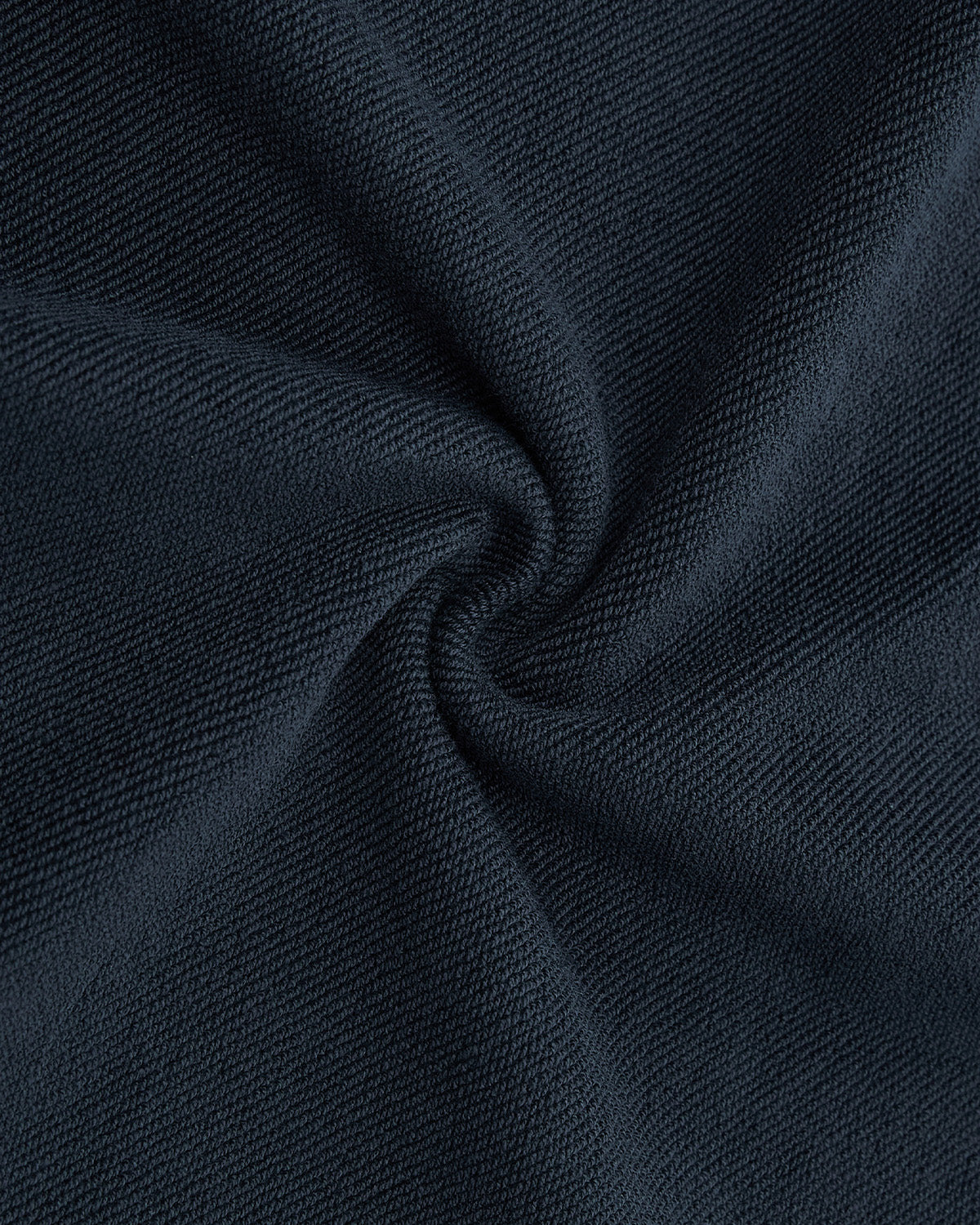 Close-up of dark textured fabric twisted in a spiral, highlighting the fine weave and soft, matte surface of Sundae School’s INDIGO WASH WRAP SWEATBAJI sweatpants.