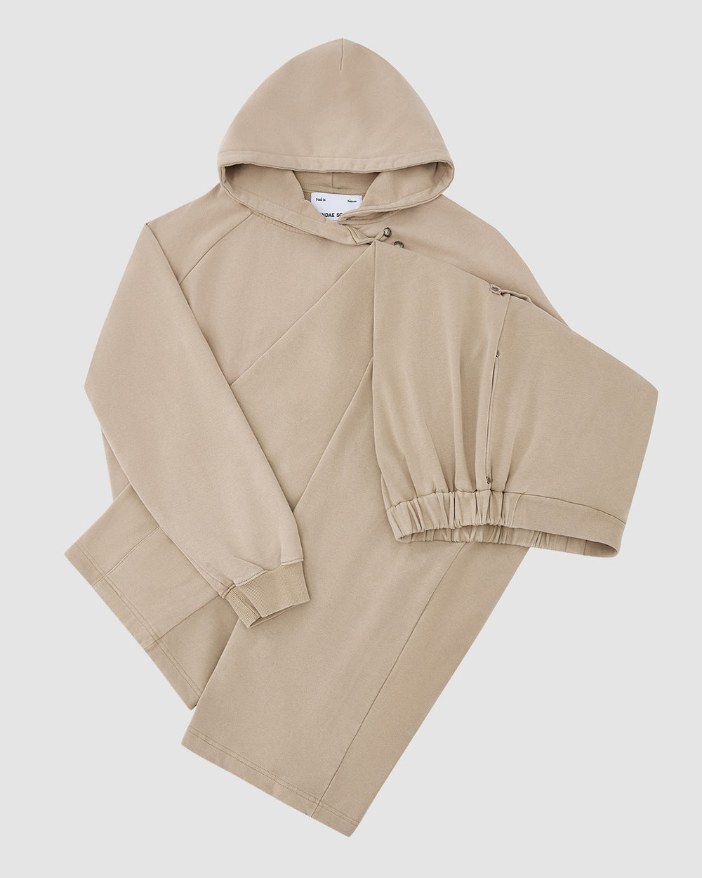 The TAUPE HANBOK HOODIE by Sundae School features a beige "떨" logo, diagonal seam design, long sleeves, one elastic cuff, and a signature sleeve stash pocket, shown laid flat on a white background.