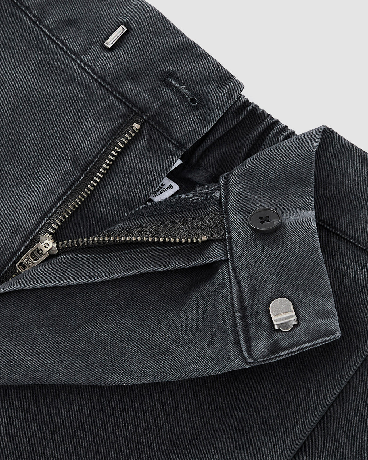 Close-up of the waistband and fly on Sundae School CHARCOAL HANBOK CHINO PANTS, showing a zipper, button, metal clasp, and belt loop detail—set against a plain light background.