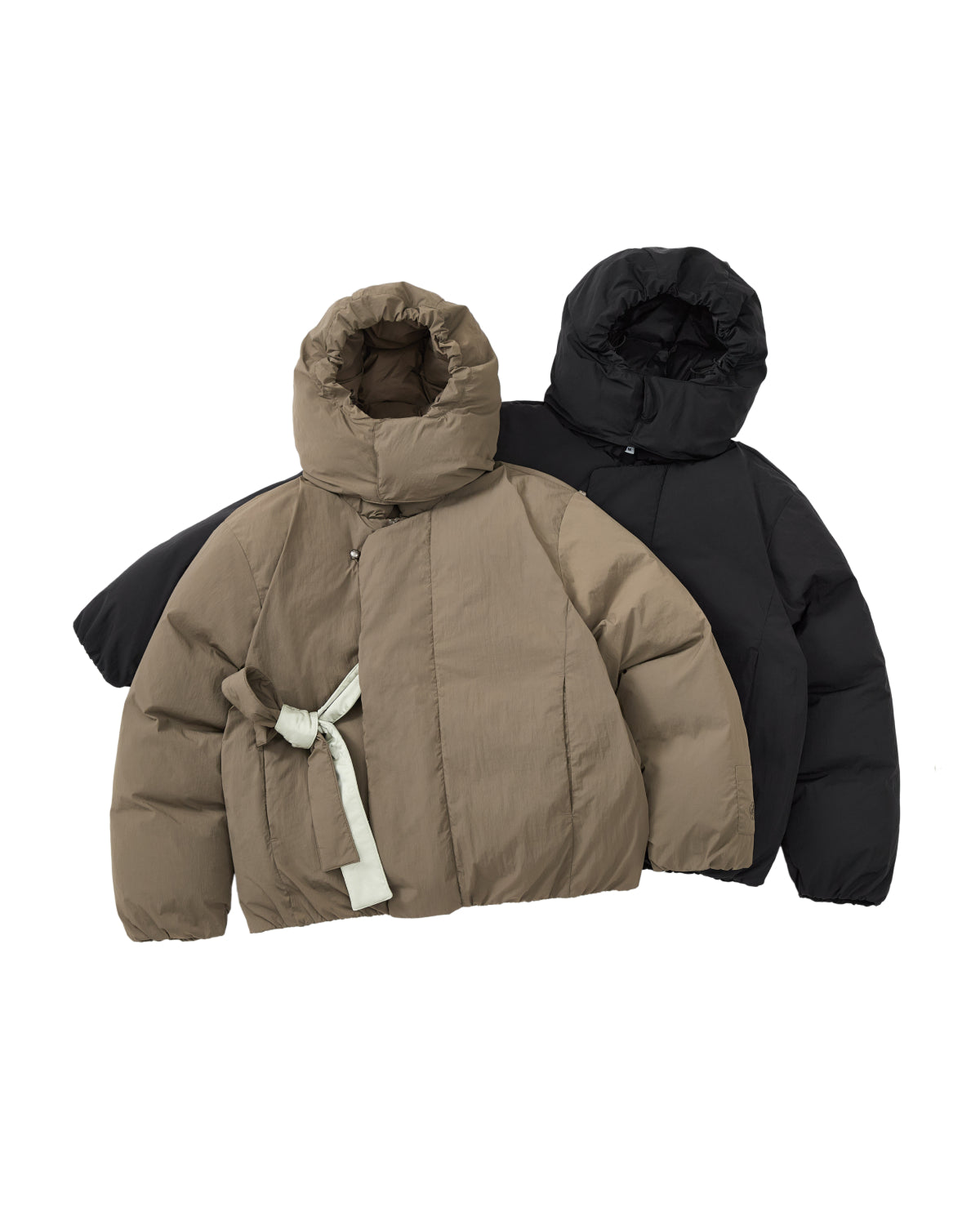 Two DEEP BROWN IBUL DOWN PUFFER jackets from Sundae School are shown lying flat on a white background: one is beige with a tied fabric belt and a high collar, and the other is black with a high collar, both featuring the cozy, cocoon-like silhouette of classic puffer styles.