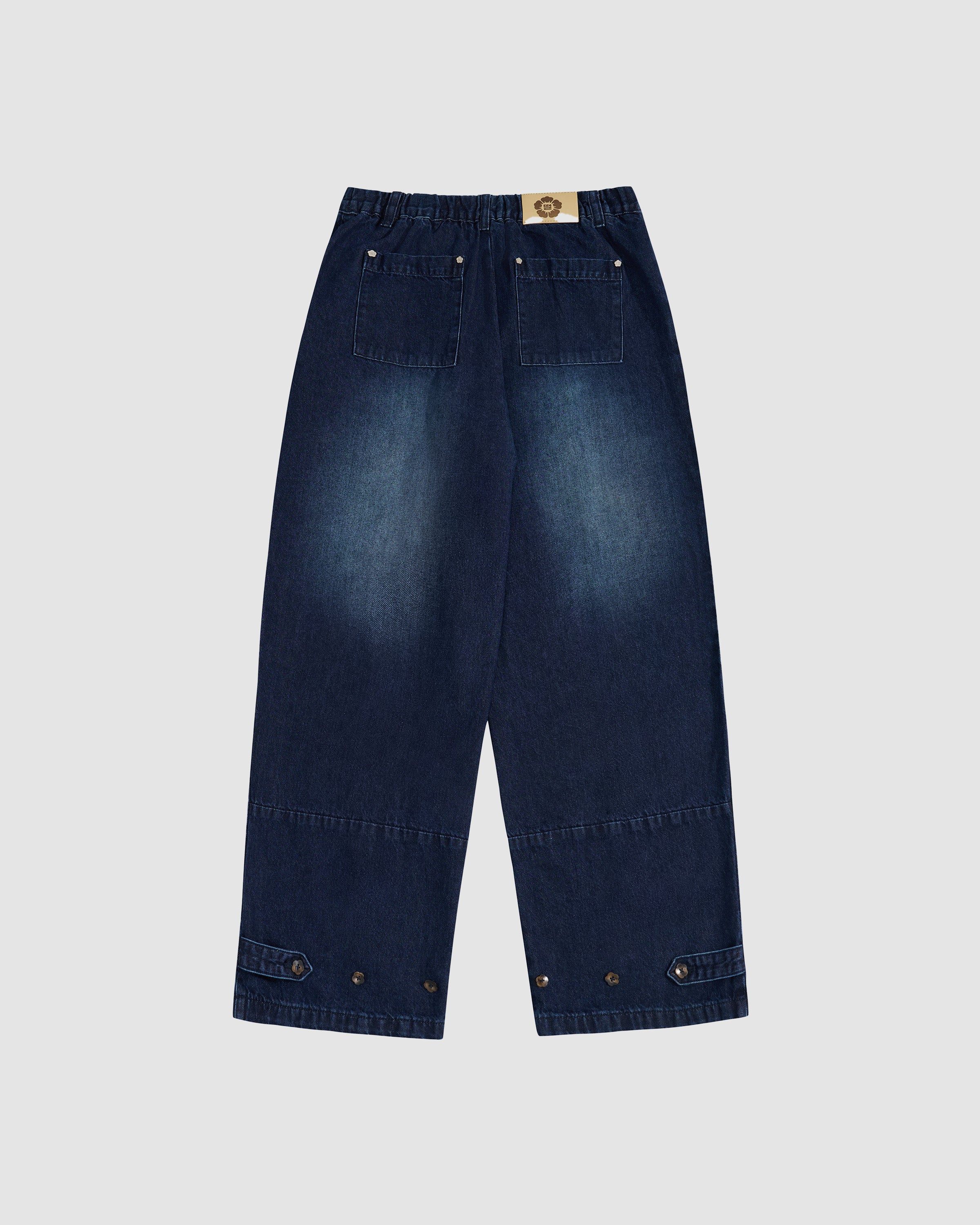 Back view flat lay of Sundae School indigo fade wide-leg hanbok denim pants showing elastic waistband, tan leather brand patch with flower logo, back pockets with silver snap button details, and wide-leg silhouette