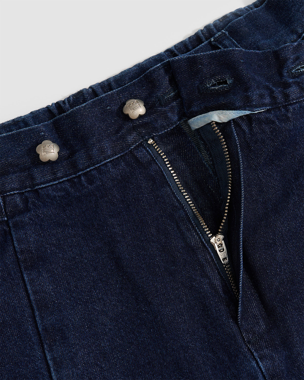 Close-up detail of indigo fade hanbok denim showing partially open zipper closure and silver flower-shaped snap button hardware, highlighting construction details and custom closure system