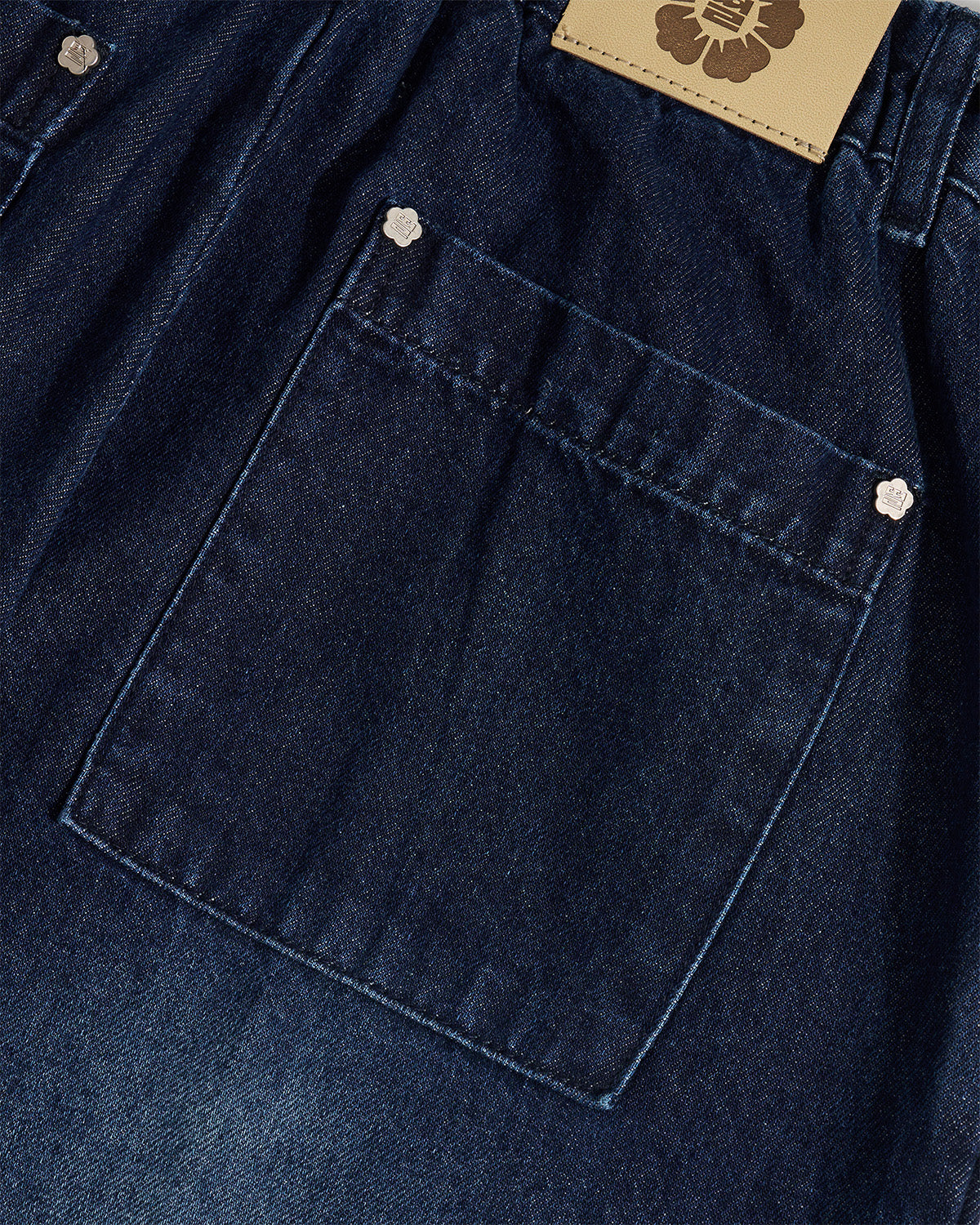 Close-up detail of indigo fade hanbok denim back pocket with silver flower-shaped snap button hardware and Sundae School leather patch visible, highlighting construction details