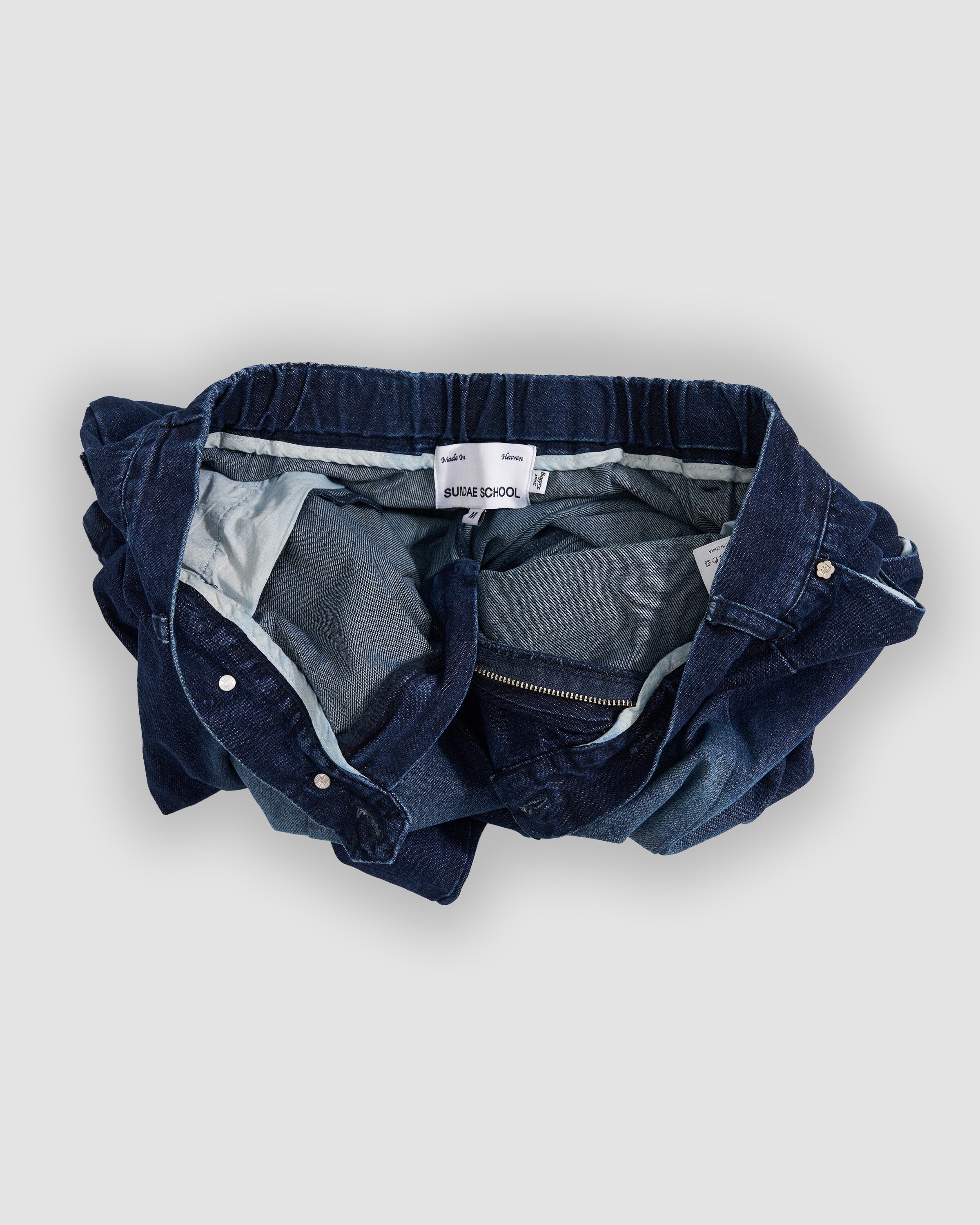 Sundae School indigo fade hanbok denim pants shown inside-out as flat lay, displaying internal construction with elastic waistband, white cotton lining, size label, and seam finishing details