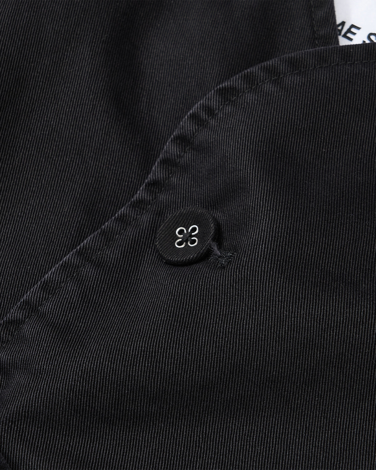 Close-up of fine ribbed black fabric with a small black button featuring a white abstract design, complementing the refined Jeogori silhouette of the Sundae School BLACK JEOGORI TIE JACKET.