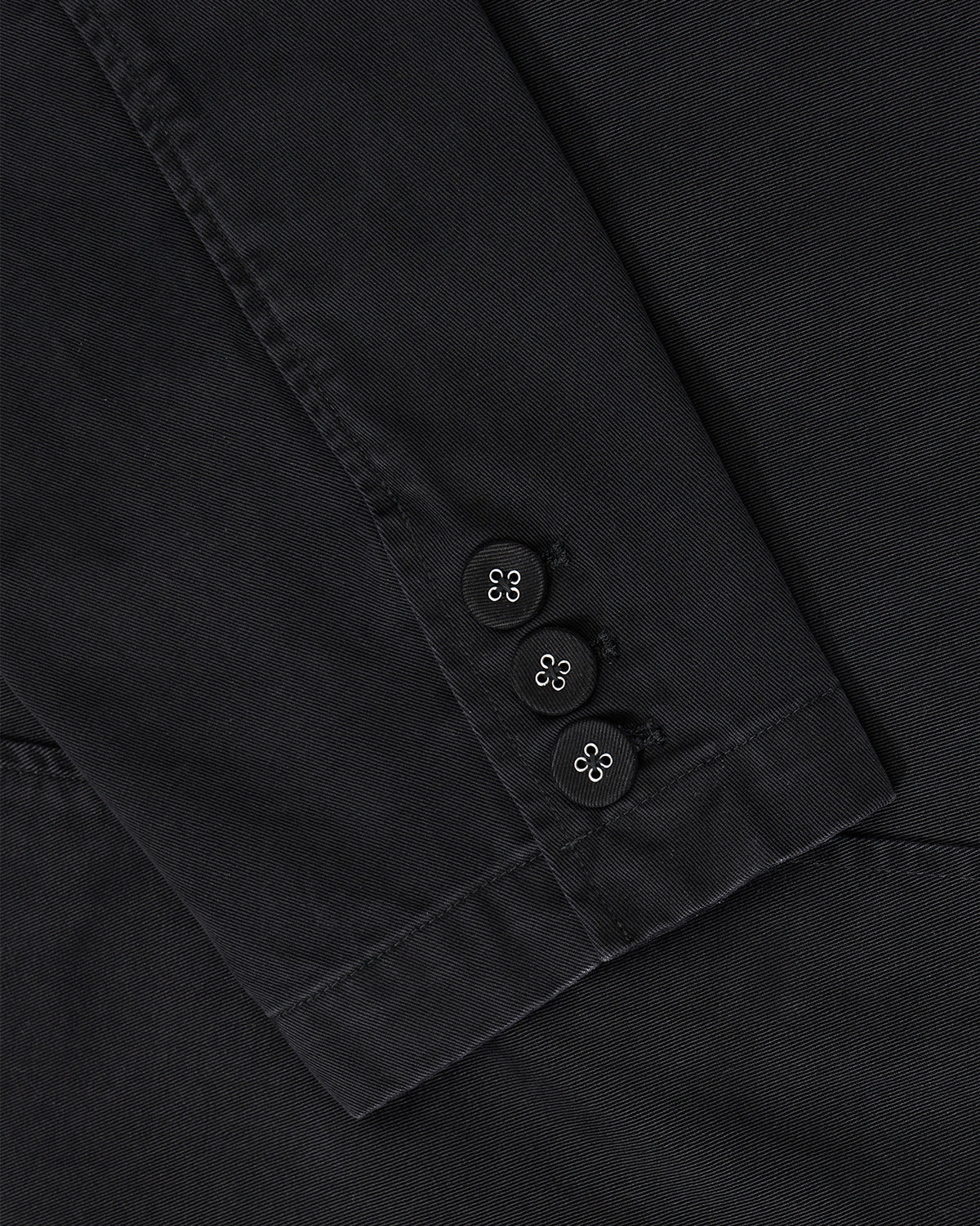 Close-up of the BLACK JEOGORI TIE JACKET by Sundae School shows a black sleeve with three black buttons and white stitching at the cuff, mirroring the refined silhouette inspired by traditional Jeogori.