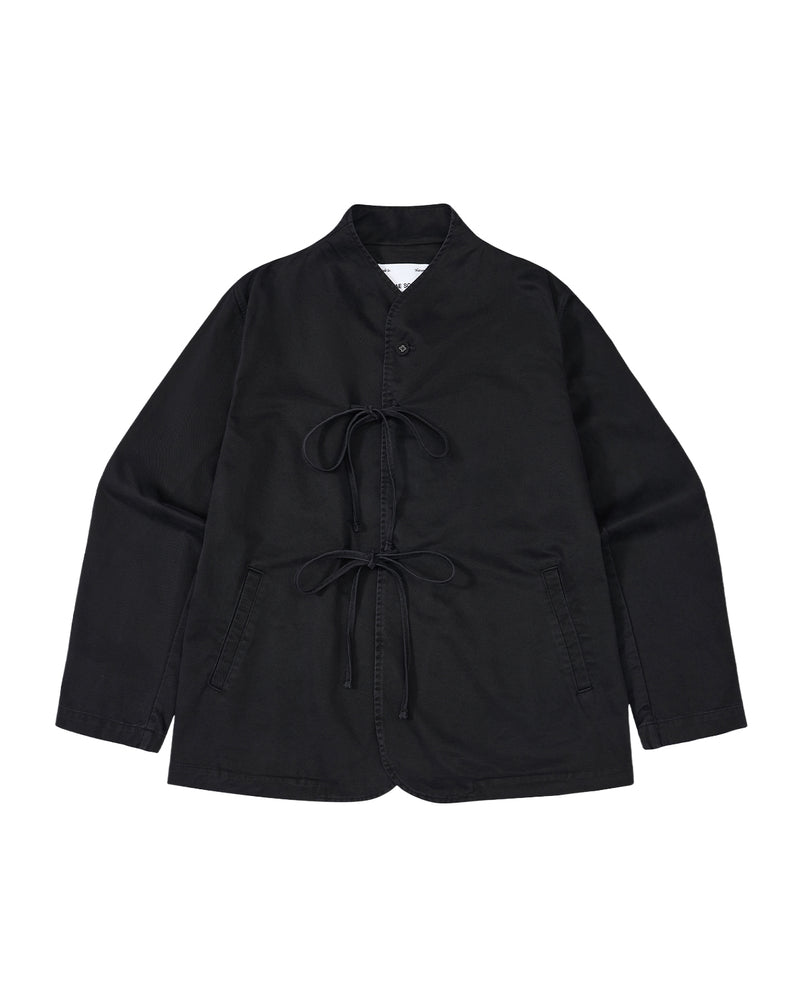 The BLACK JEOGORI TIE JACKET by Sundae School features a monk collar, jeogori-inspired design, two front pockets, and double goreum tie closures. Made from lightweight chino fabric, the jacket is displayed laid flat on a white background.
