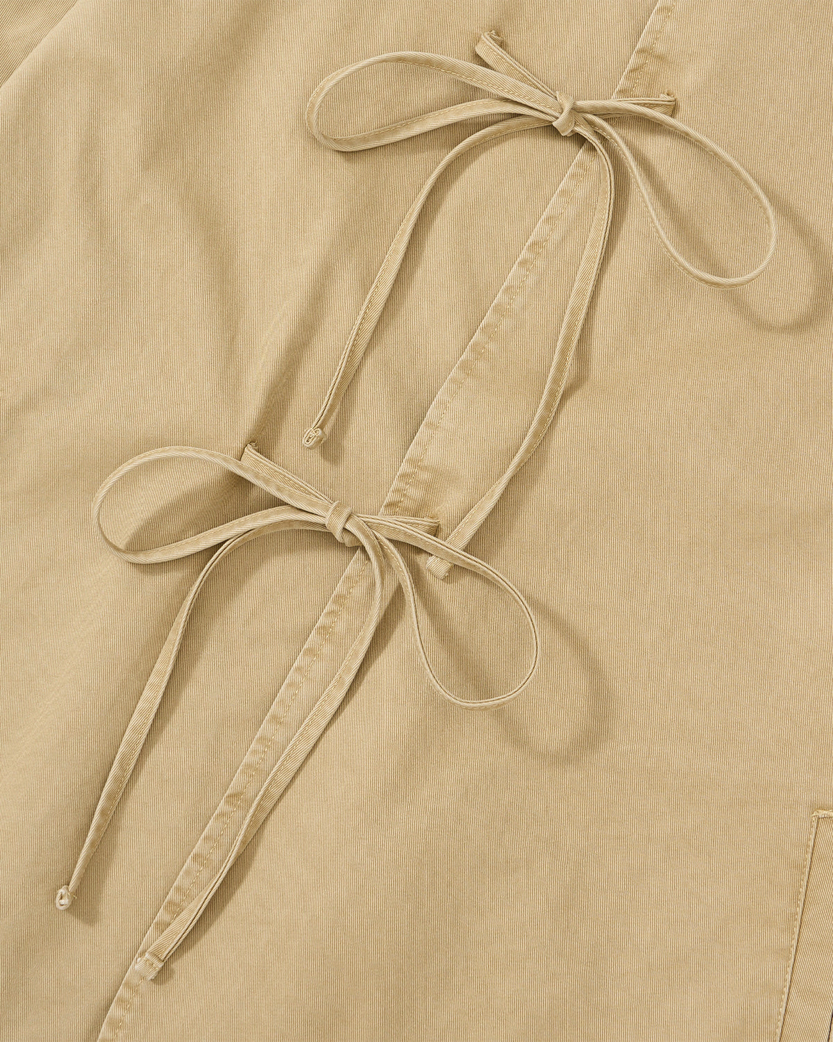 Close-up of Sundae School's TAN JEOGORI TIE JACKET shows beige fabric with two matching drawstring bows along the edge, adding elegant detail inspired by the classic jeogori silhouette.