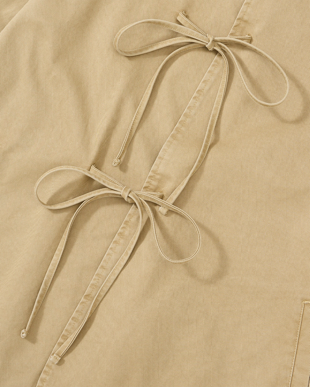 Close-up of the Sundae School TAN JEOGORI TIE JACKET, featuring beige fabric accented with two bows crafted from slender fabric strips and attached along a stitched seam—a nod to the traditional detailing found on summer suiting or the classic jeogori.